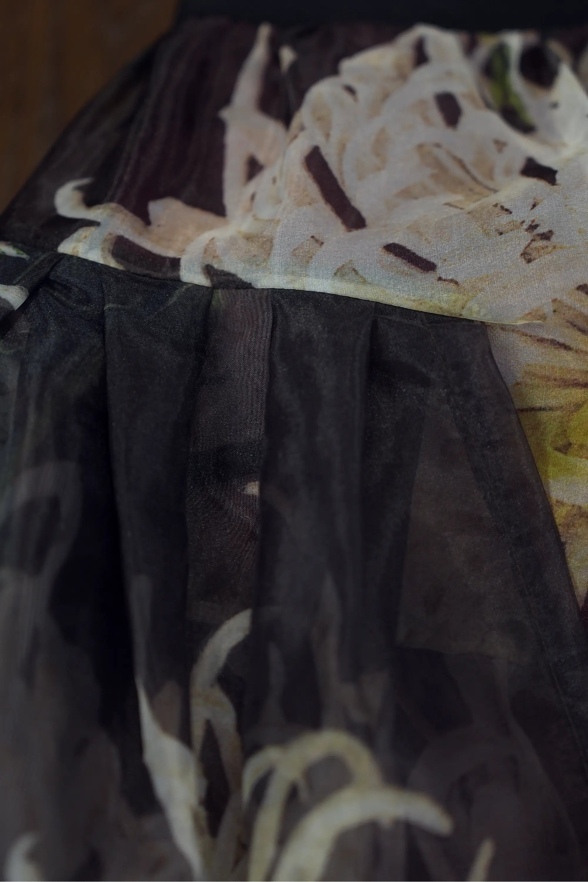 Close-up of sheer floral skirt detailing layered overlay and soft pleating, highlighting lightweight transparency, fluid drape, and the interplay between printed fabric and darker sheer layer beneath