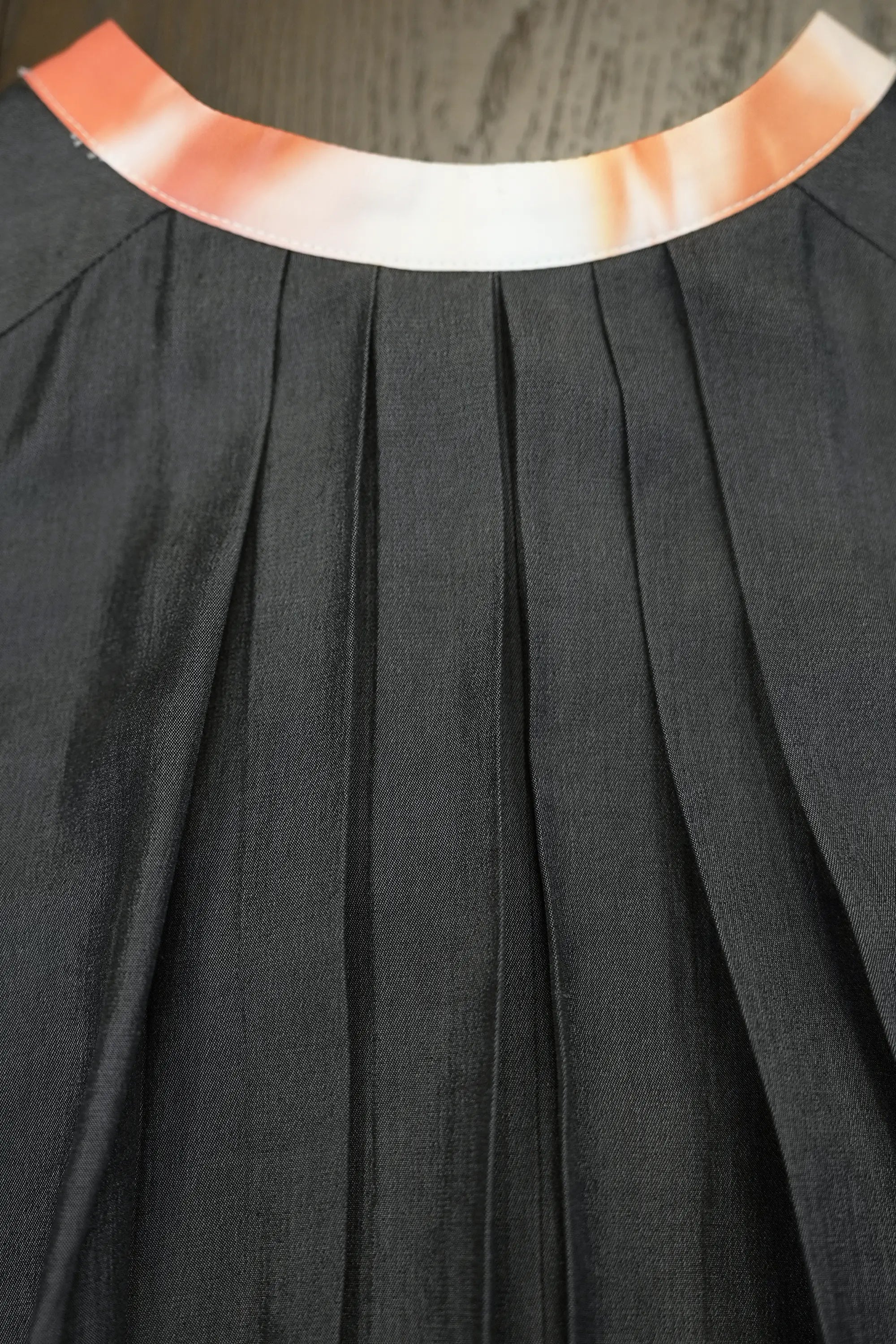 Close-up of charcoal dress showcasing structured pleats beneath a printed micro Chinese collar neckline, highlighting clean tailoring, soft volume, and smooth fabric drape