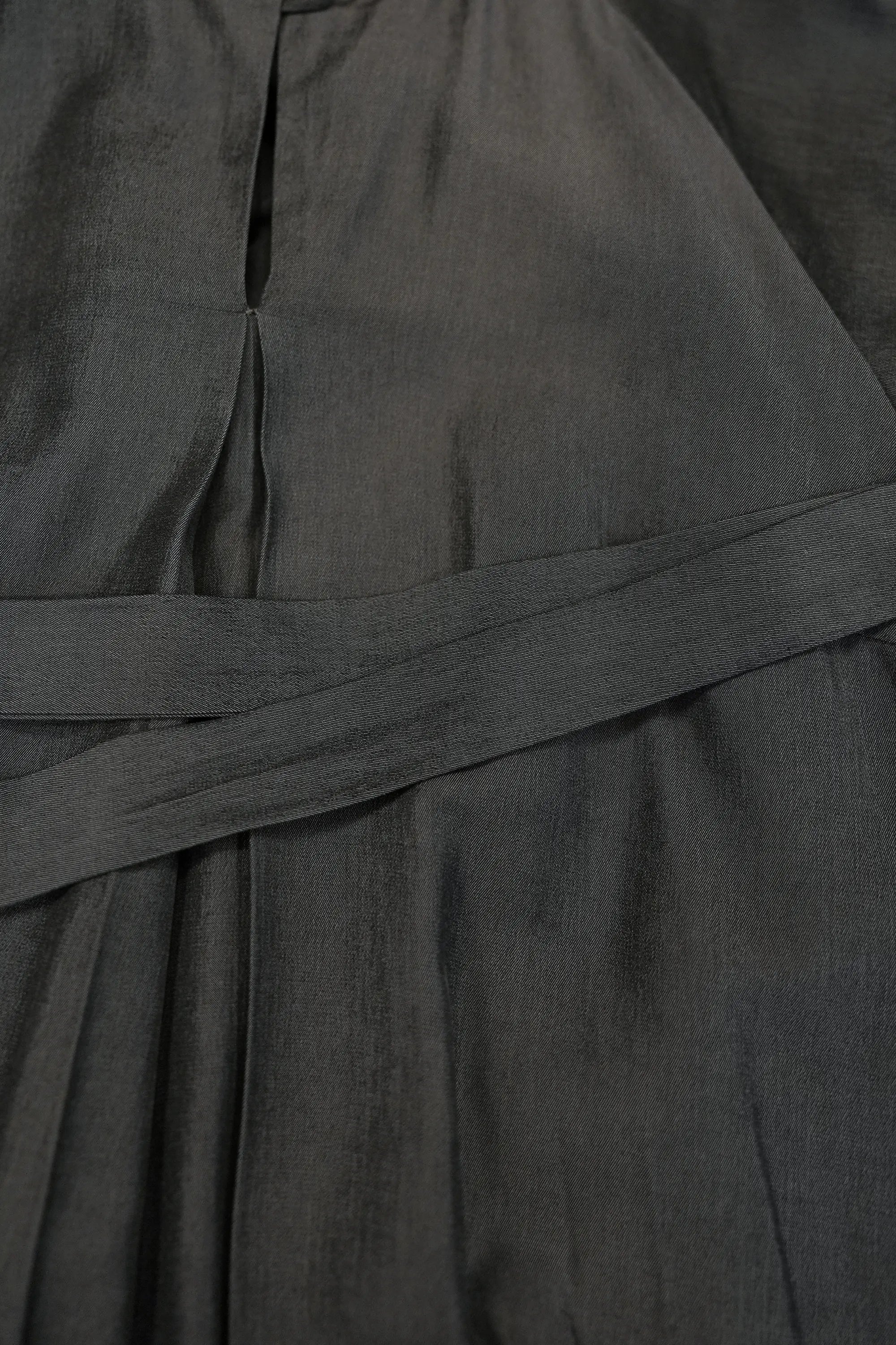 Close-up of charcoal dress highlighting adjustable waist sash tie, showcasing fine texture, clean seam lines, and softly gathered fabric for a refined, structured drape