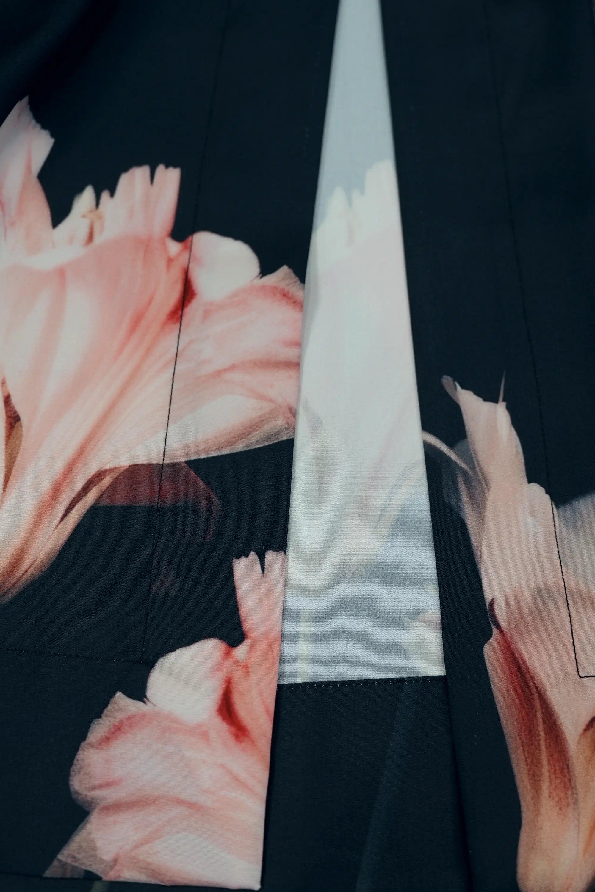 Close-up of dark pleated slit pants highlighting vertical slit detail with contrast inner panel, and pink floral placement print, showcasing fluid movement and refined construction