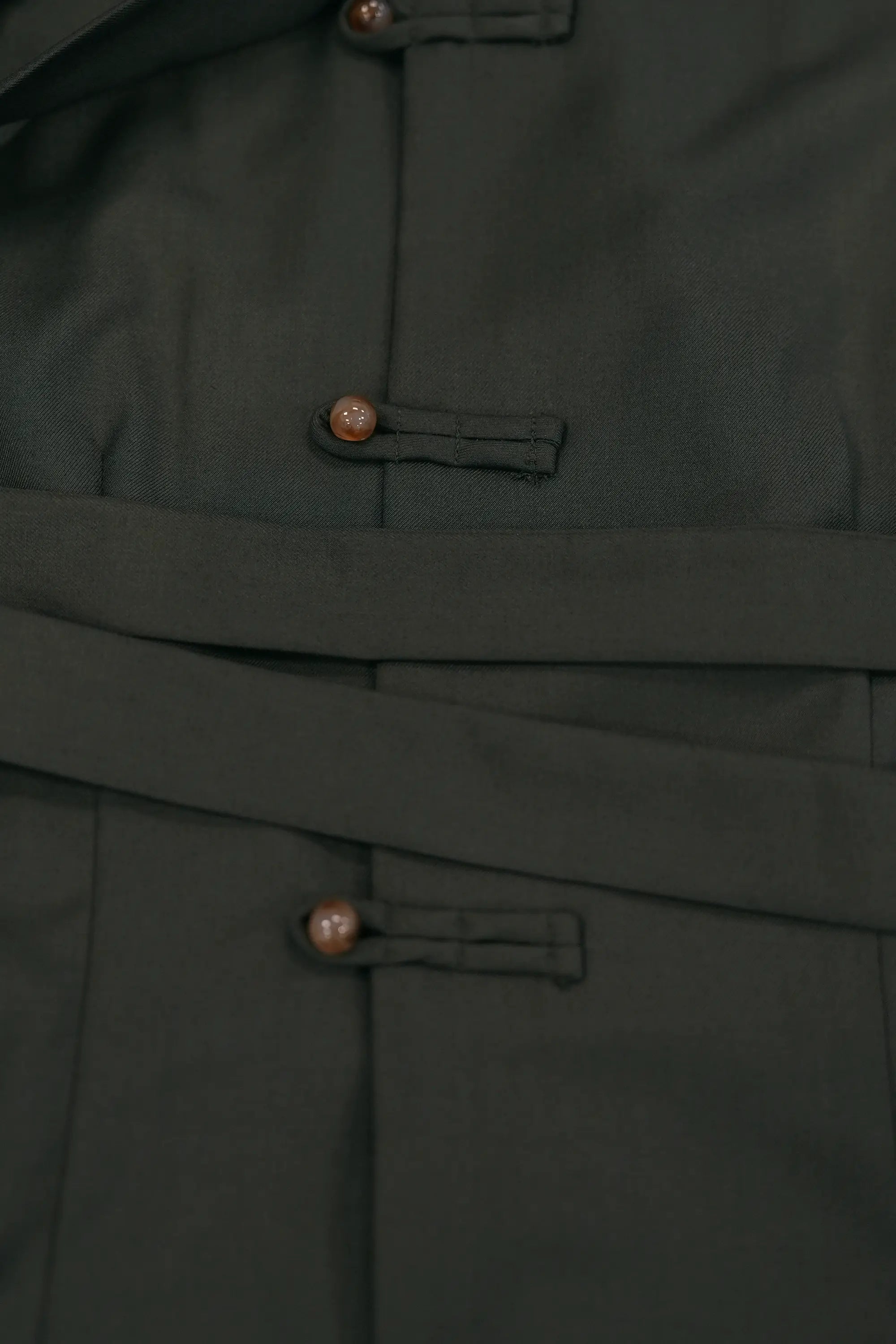 Close-up of deep green top showcasing pankou button closures and adjustable waist sash, highlighting refined stitching, smooth fabric finish, and structured tailoring