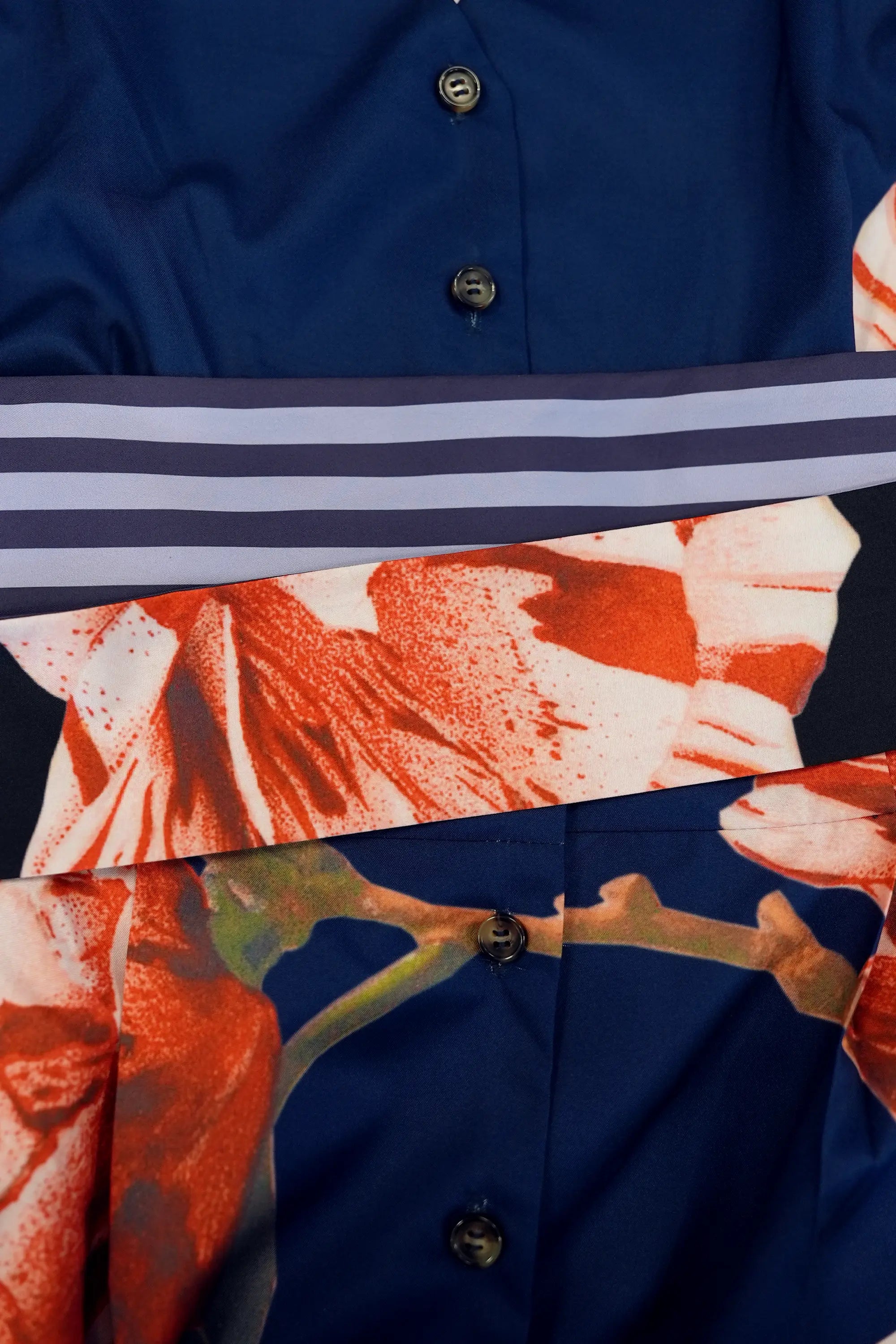 Close-up of contrast sash detail on navy dress, featuring layered striped and floral print panels tied at the waist, with button-down front and structured tailoring visible underneath