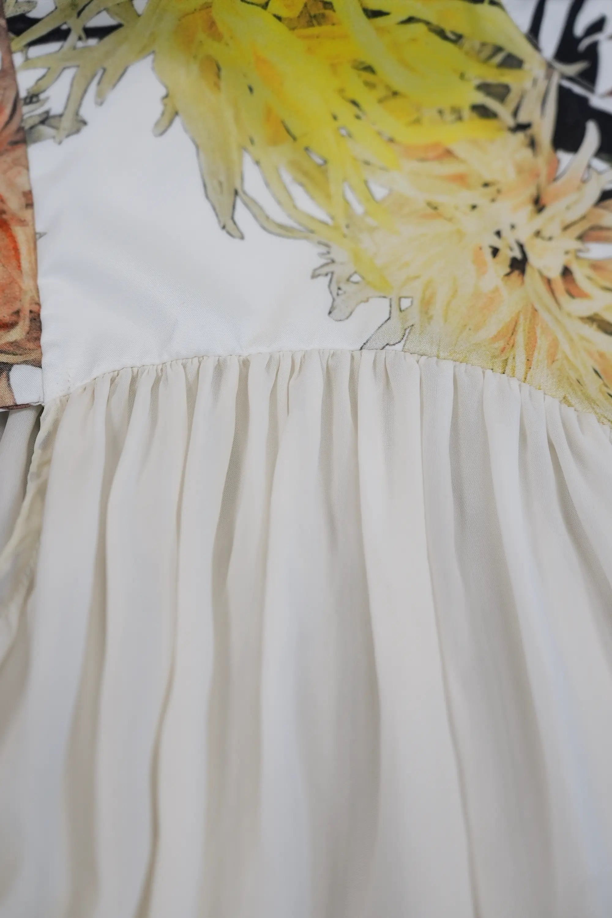 Close-up of softly gathered white fabric flowing from the printed yoke, showcasing fine pleating and a fluid, airy drape for gentle movement