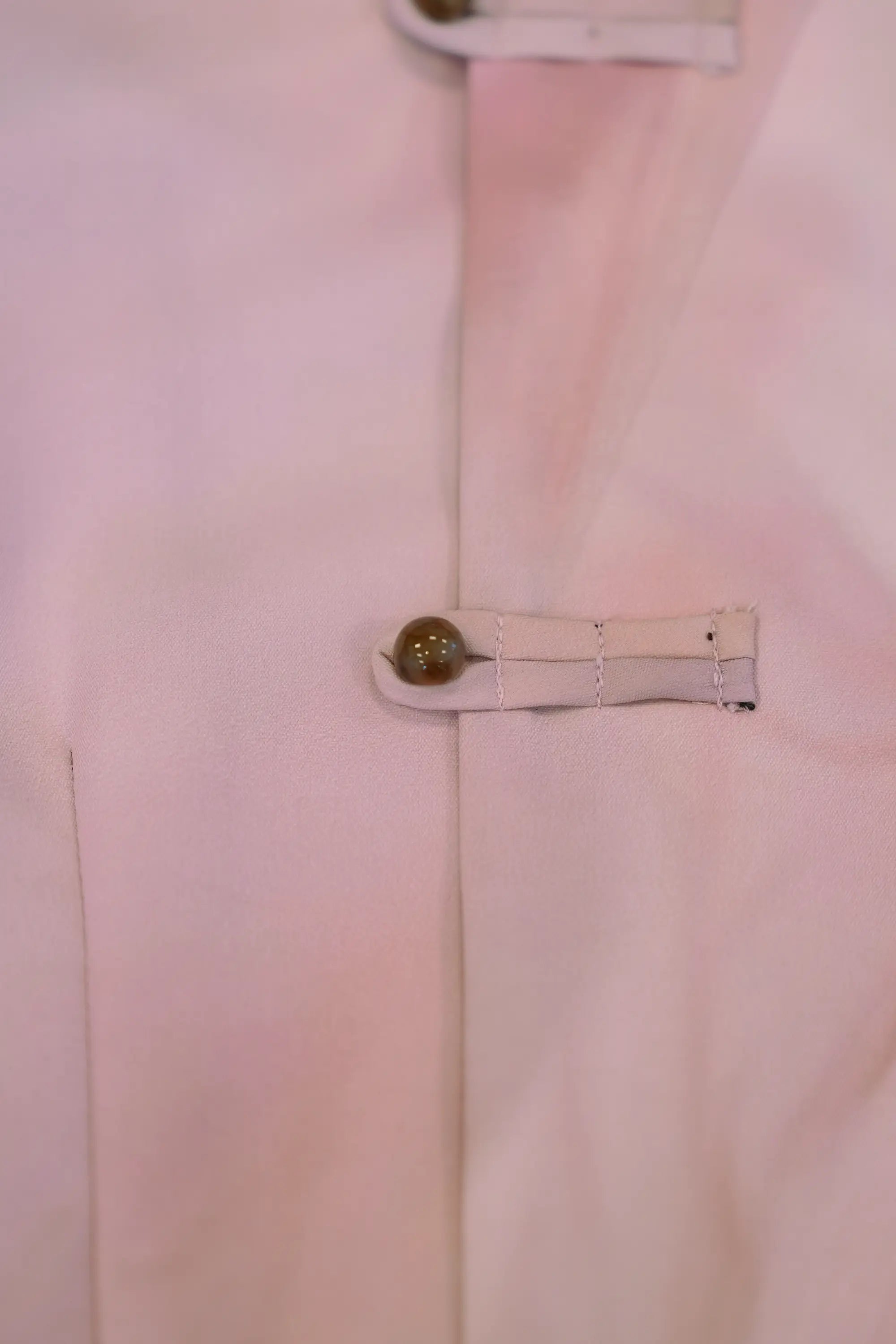 Close-up of blush pink top featuring traditional Chinese pankou closure, highlighting fabric loops, rounded button detail, and smooth lightweight material with clean seam finishing
