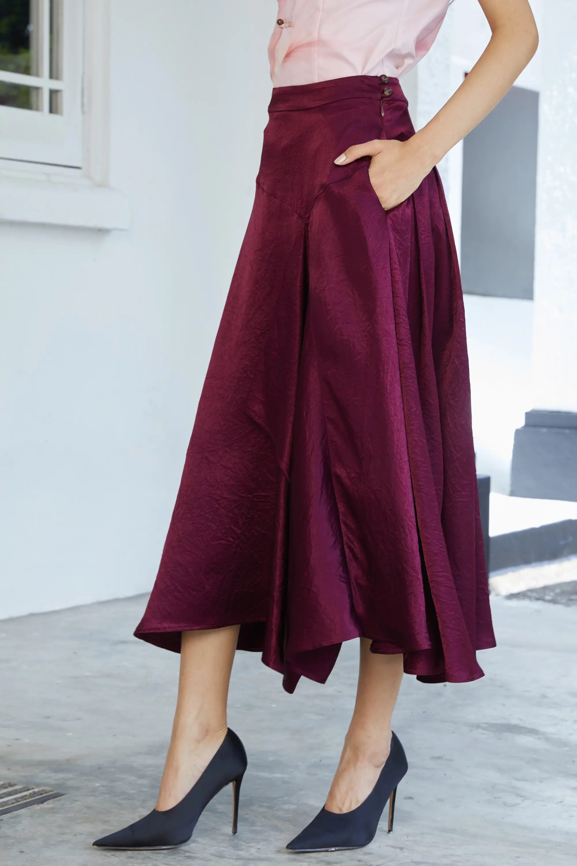 Side view of burgundy skirt with soft drape, cascading panel detail and elegant movement