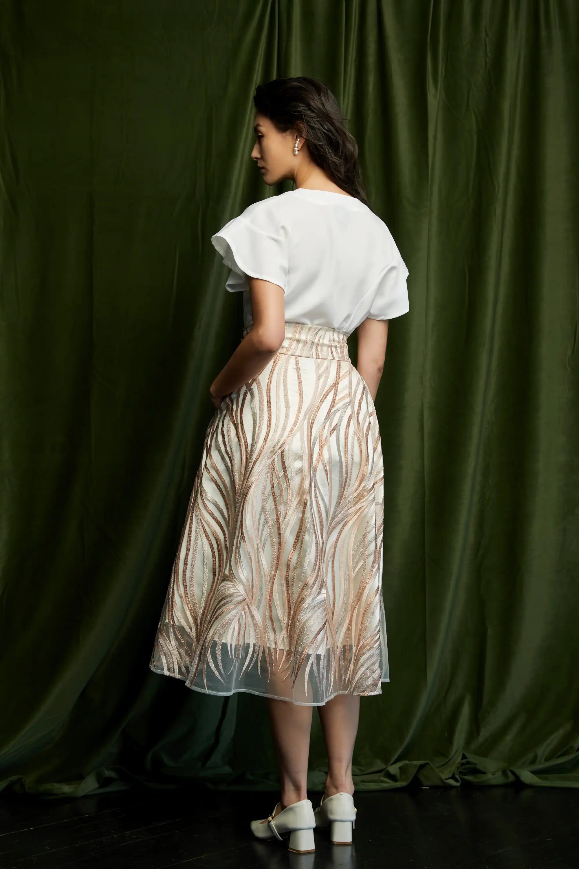 White peplum blouse with flutter sleeves and soft drape paired with sheer embroidered lace midi skirt, full back view