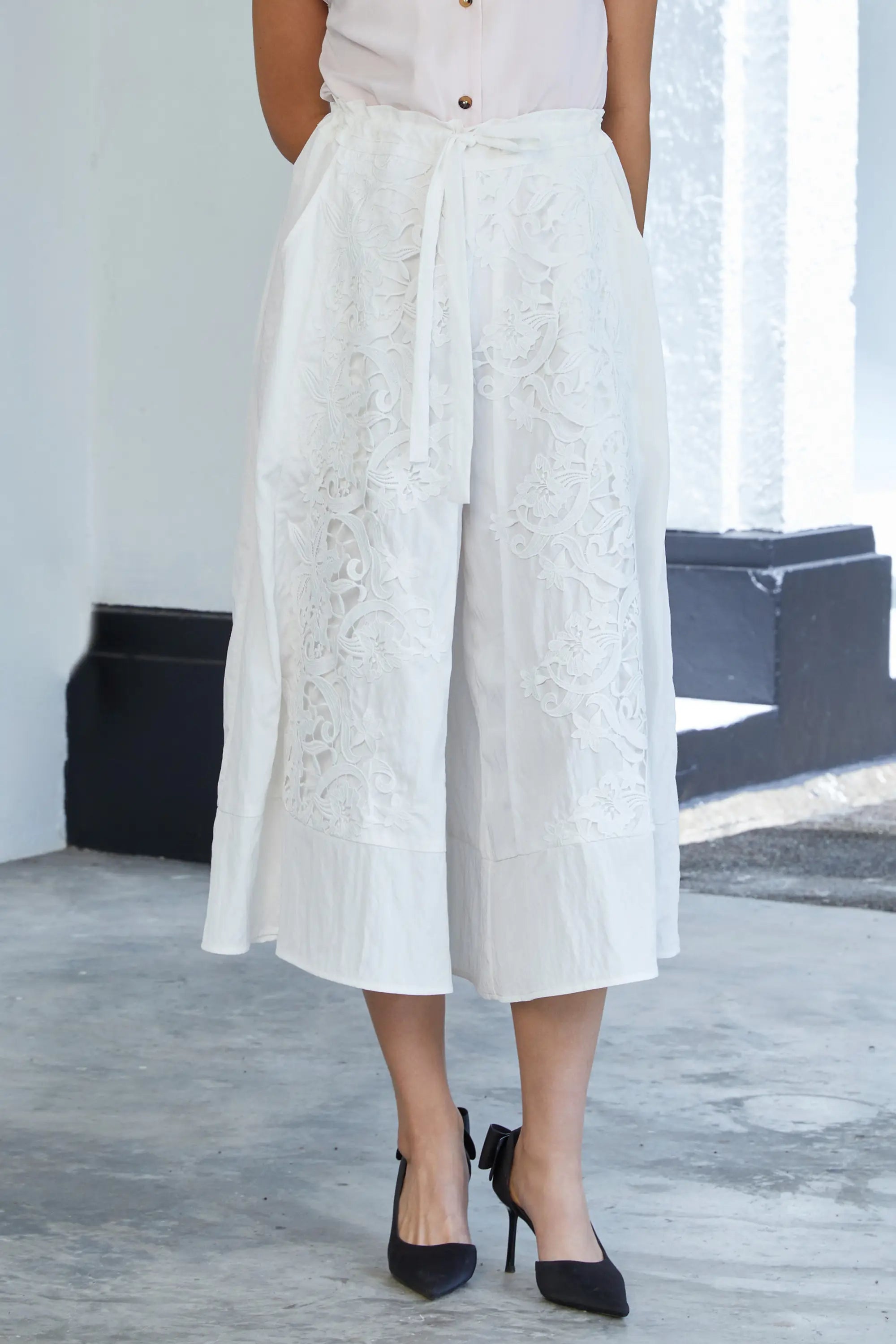 Woman wearing ABIDE white lace wide-leg cropped pants with waist tie (front view)