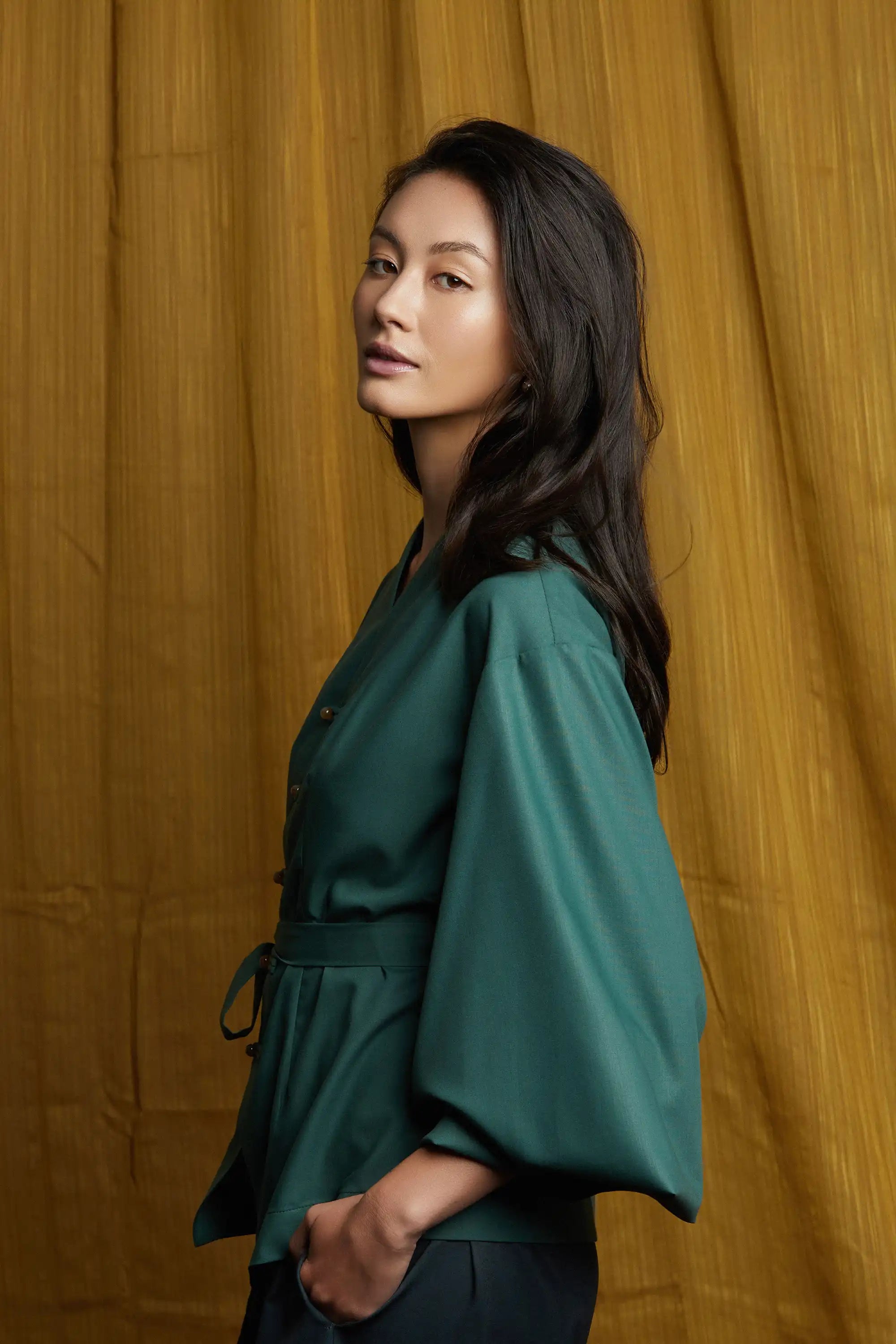 Deep green top with clean side profile, fluid sleeves, and waist-cinching sash tie that enhances shape and movement