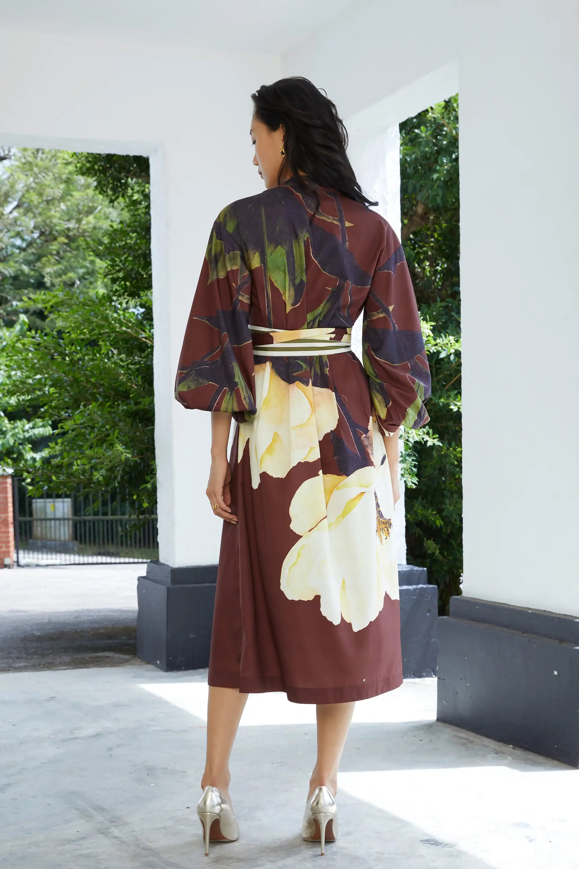 Woman wearing ABIDE brown floral midi dress with contrast sash belt (back view)