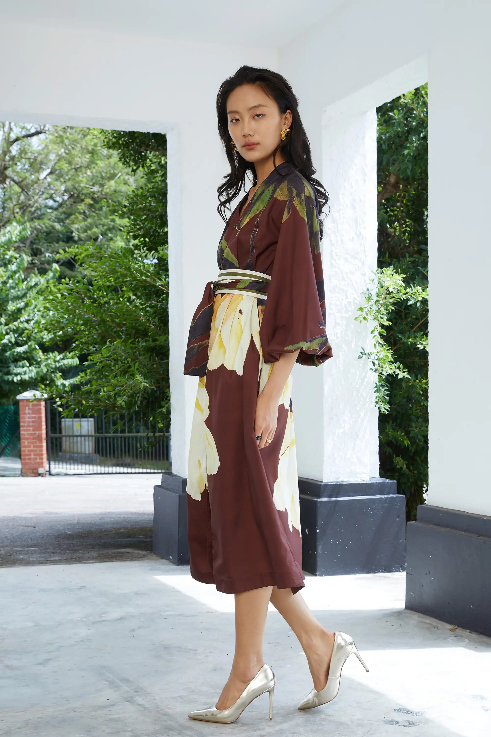 Woman wearing ABIDE brown floral midi dress with contrast sash belt (side view)