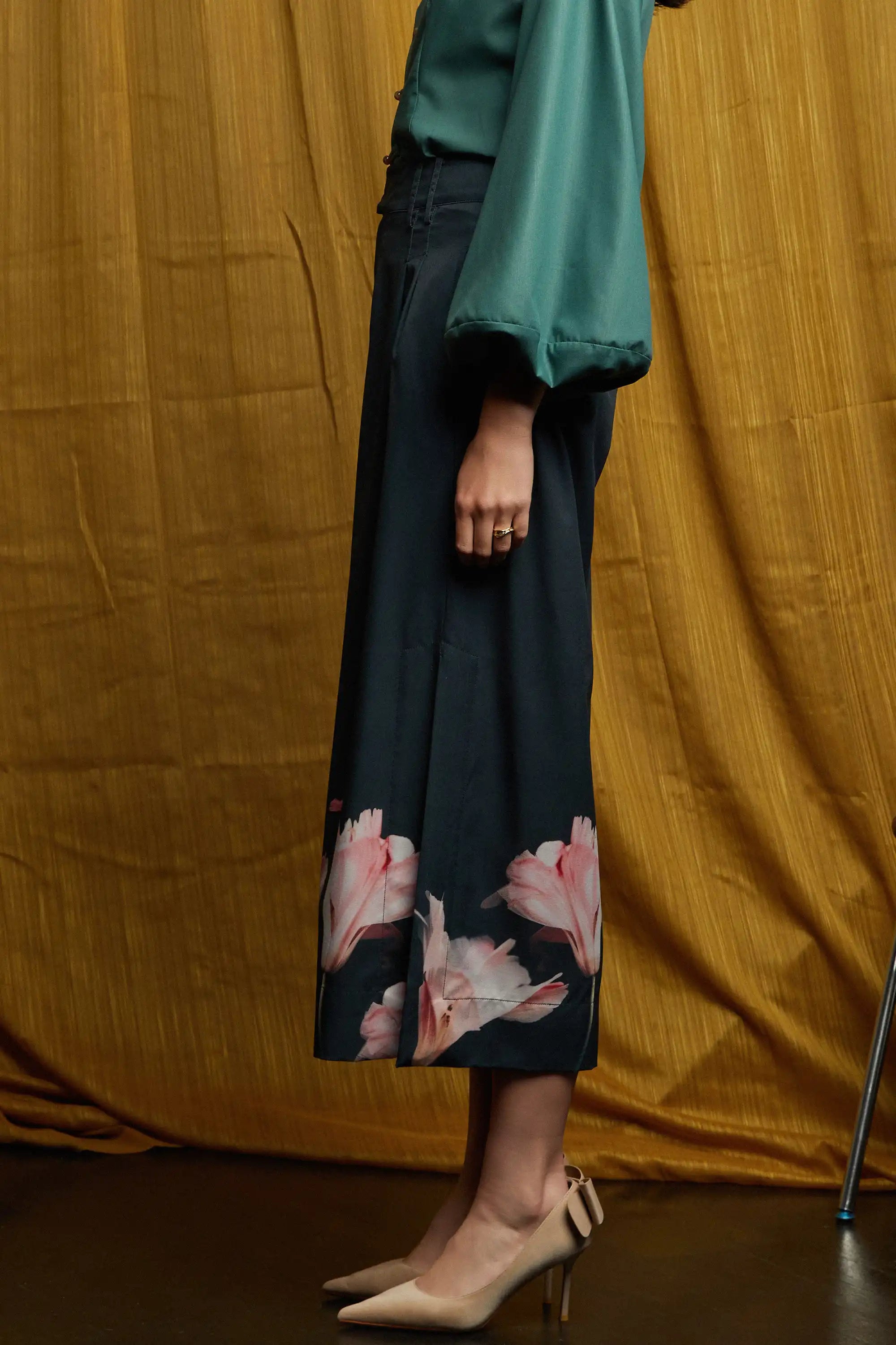 Deep green long-sleeve top with fluid sleeves and clean side profile, paired with dark pleated slit pants with gentle drape, side pockets, and subtle volume through pleating