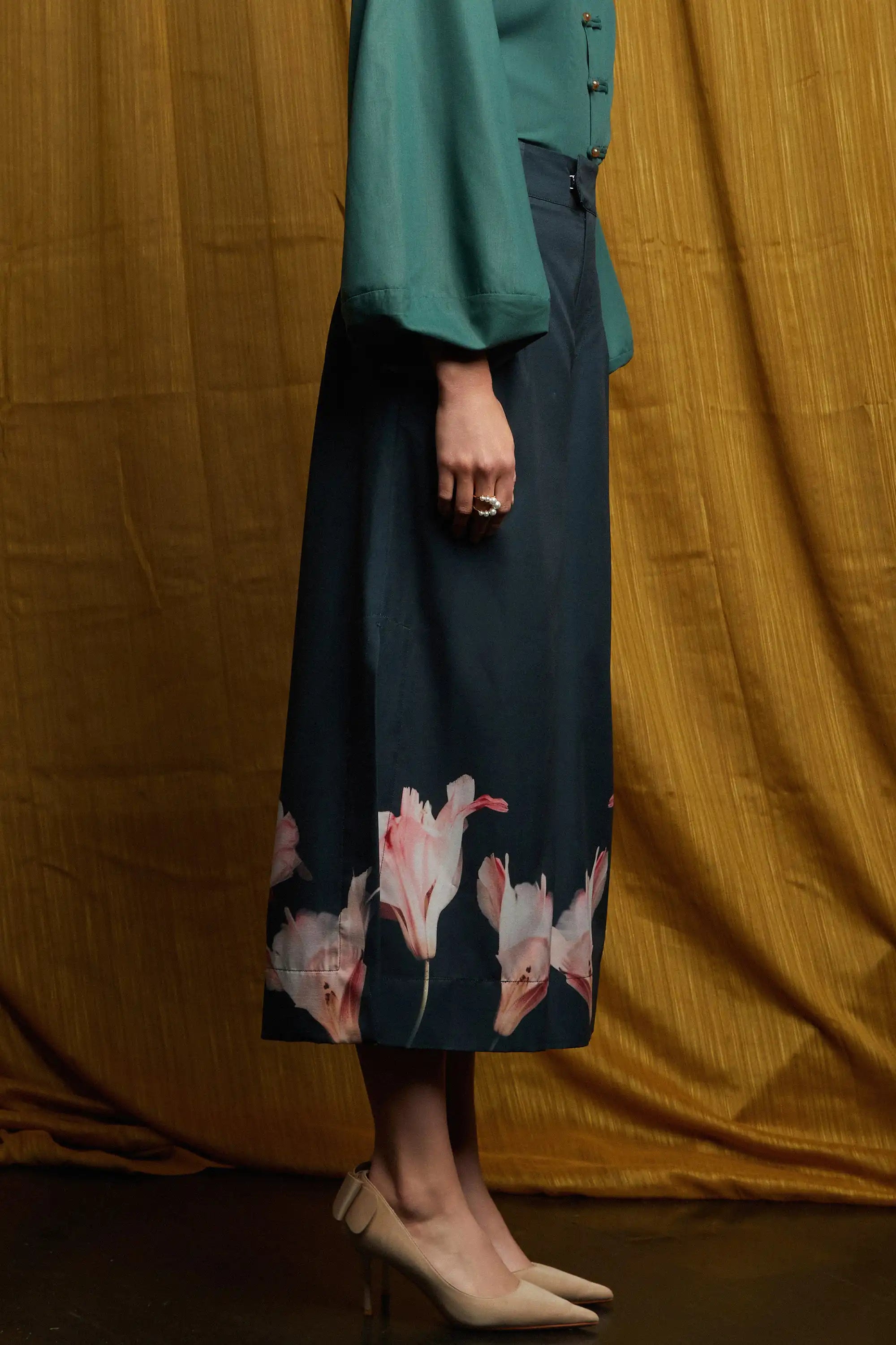 Deep green long-sleeve top with fluid sleeves and clean side profile, paired with dark pleated slit pants with gentle drape, side pockets, and subtle volume through pleating