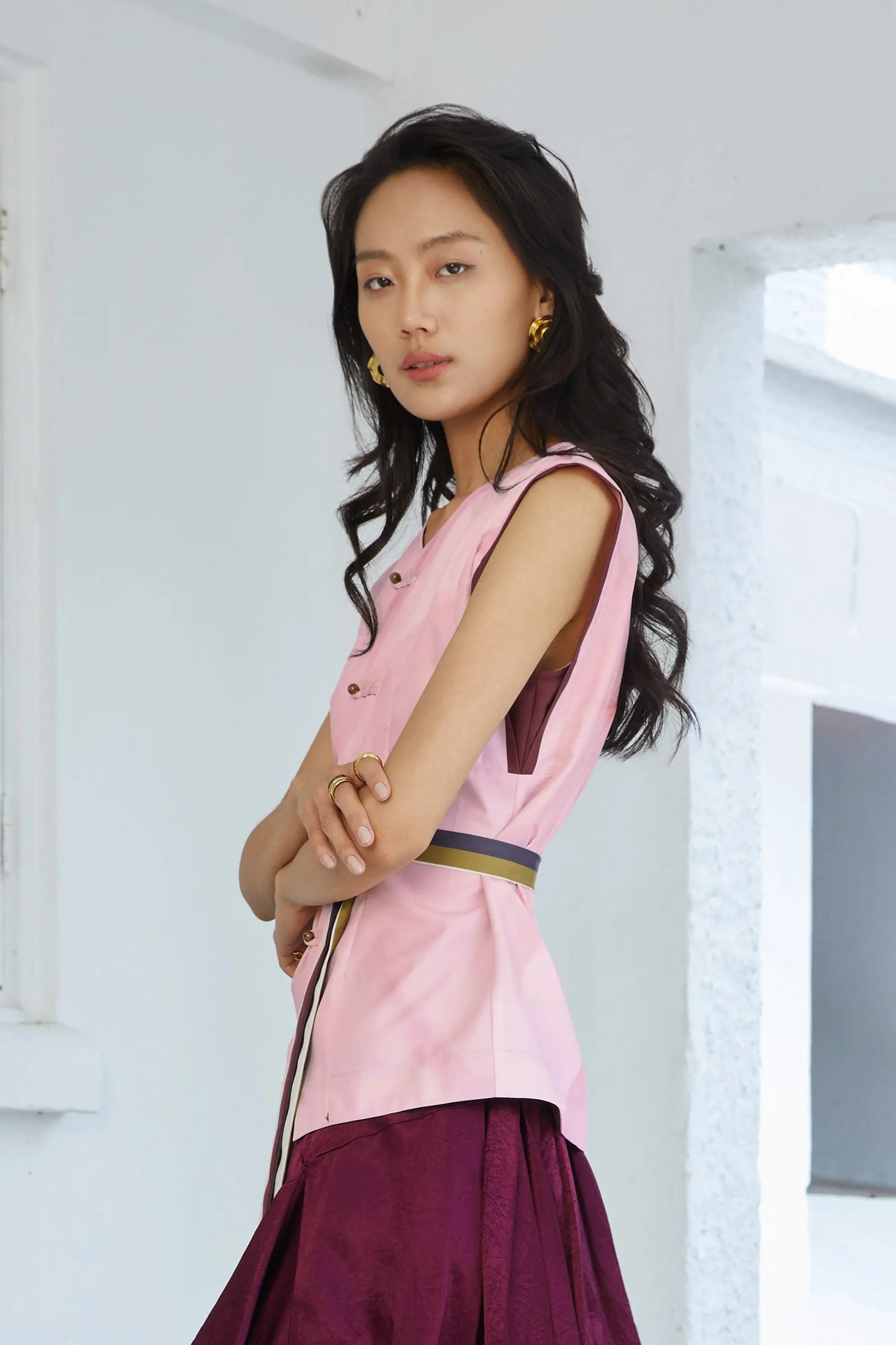 Side profile of blush pink square sleeves top with structured silhouette, contrast piping, and adjustable sash belt defining the waist, styled with a wine skirt.