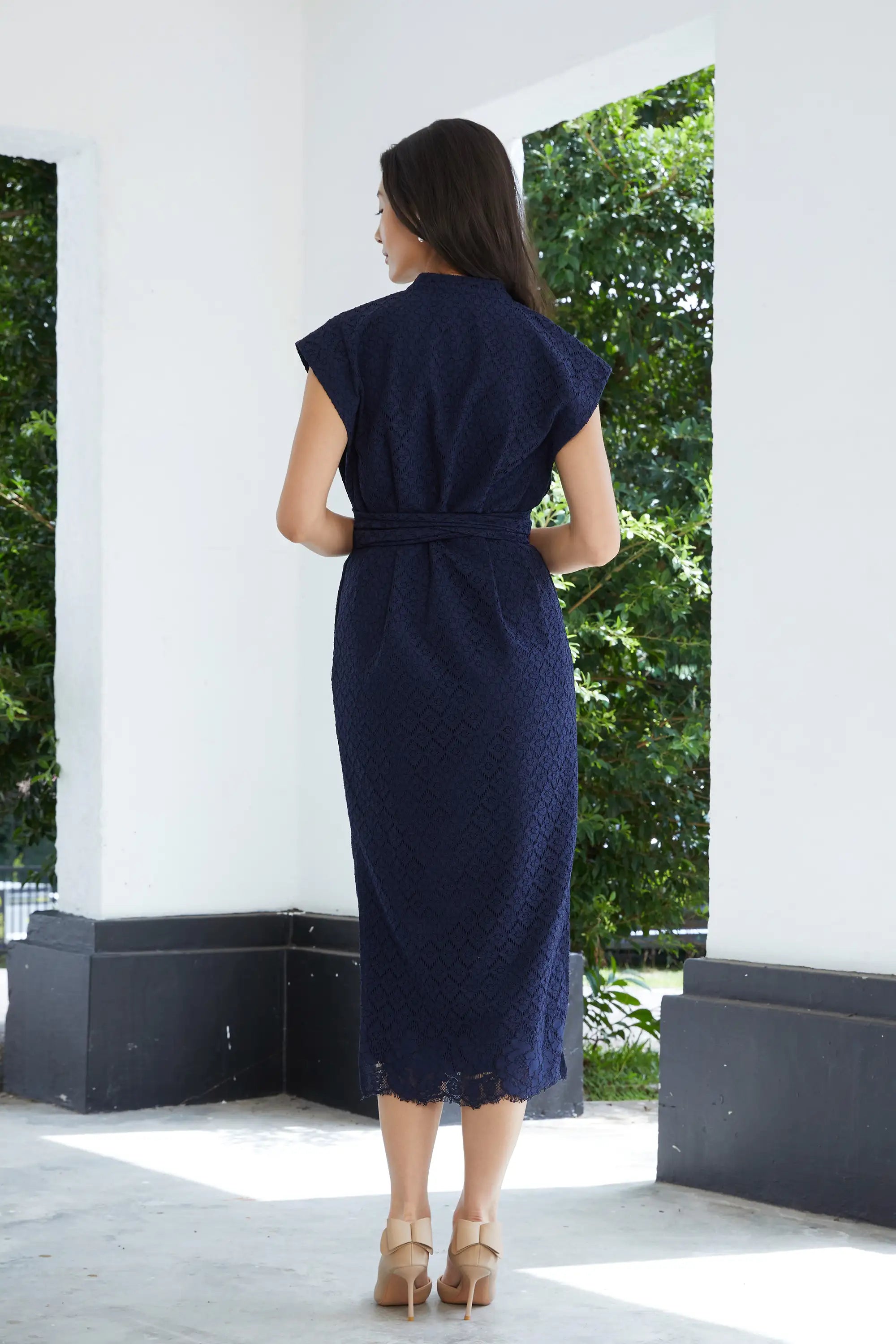 Woman wearing ABIDE navy lace midi dress with fitted silhouette and waist tie (back view)