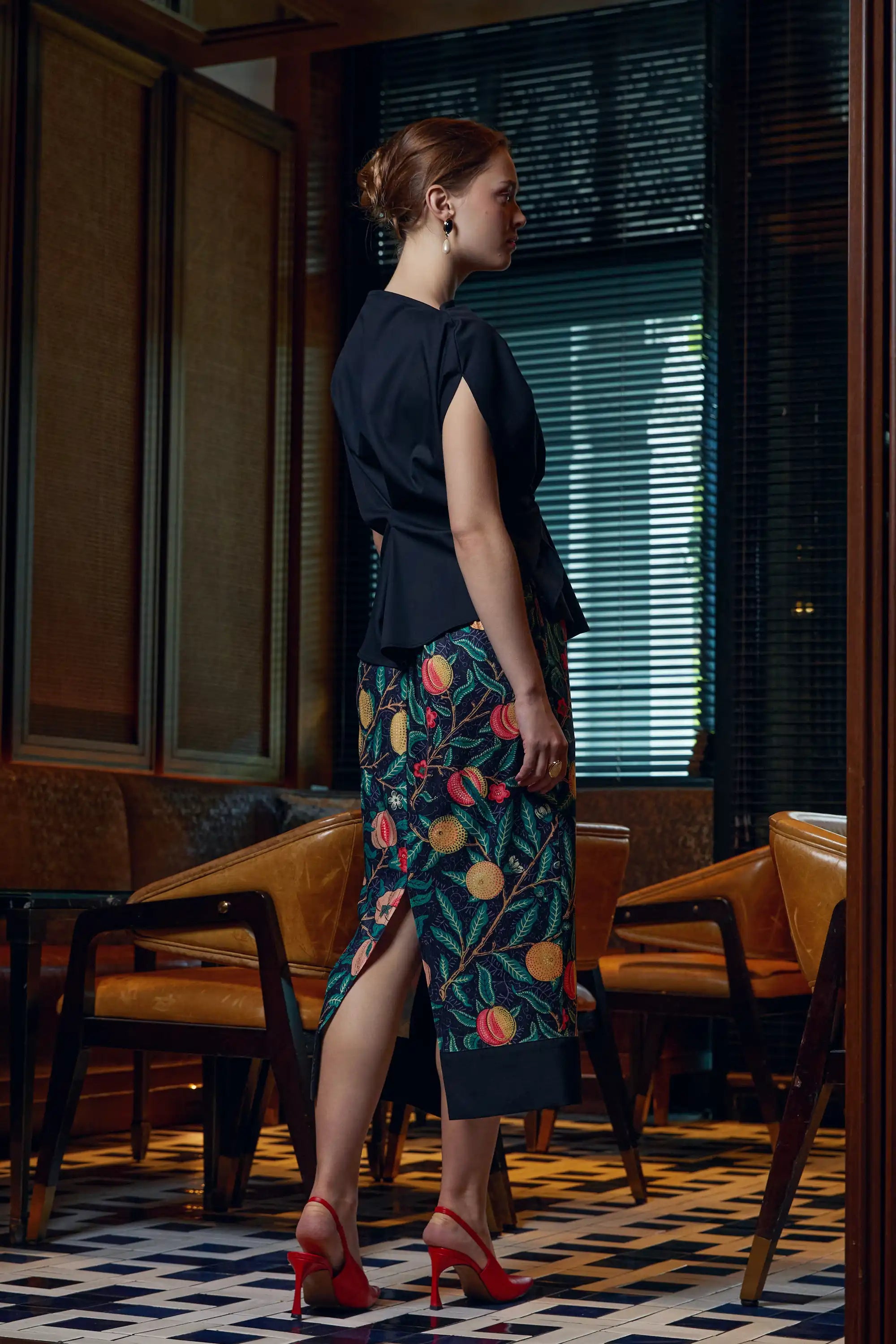 Woman wearing adjustable black top with Arrayed Pomegranate print ribbed midi skirt, side view