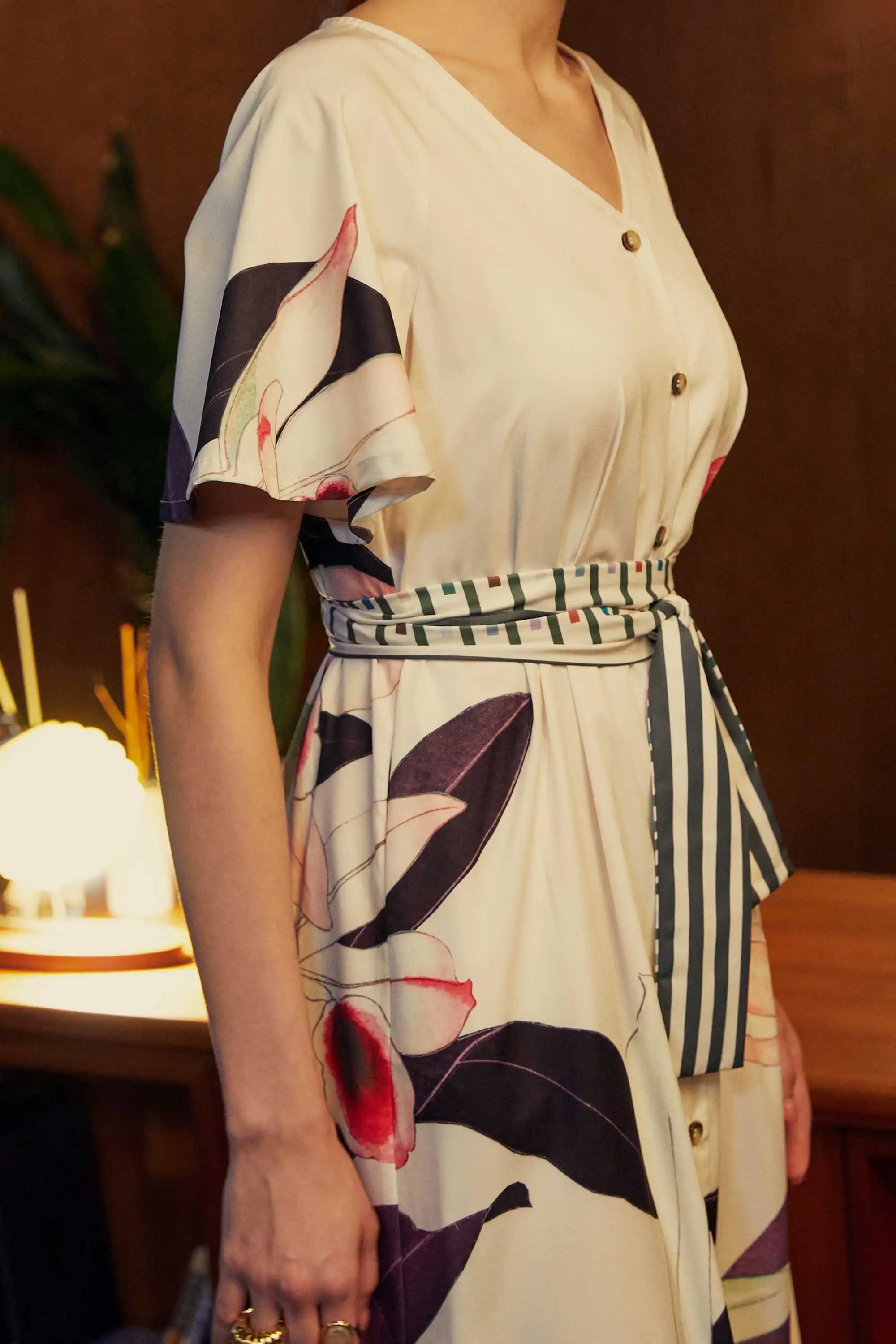 Close-up of the BEHOLD Flutter Sleeves Box Pleats Cinch Midi Dress in Dendrobium orchid print, highlighting cream fabric with bold floral motifs, striped cinched waist tie, V-neckline, and flutter sleeve detail.