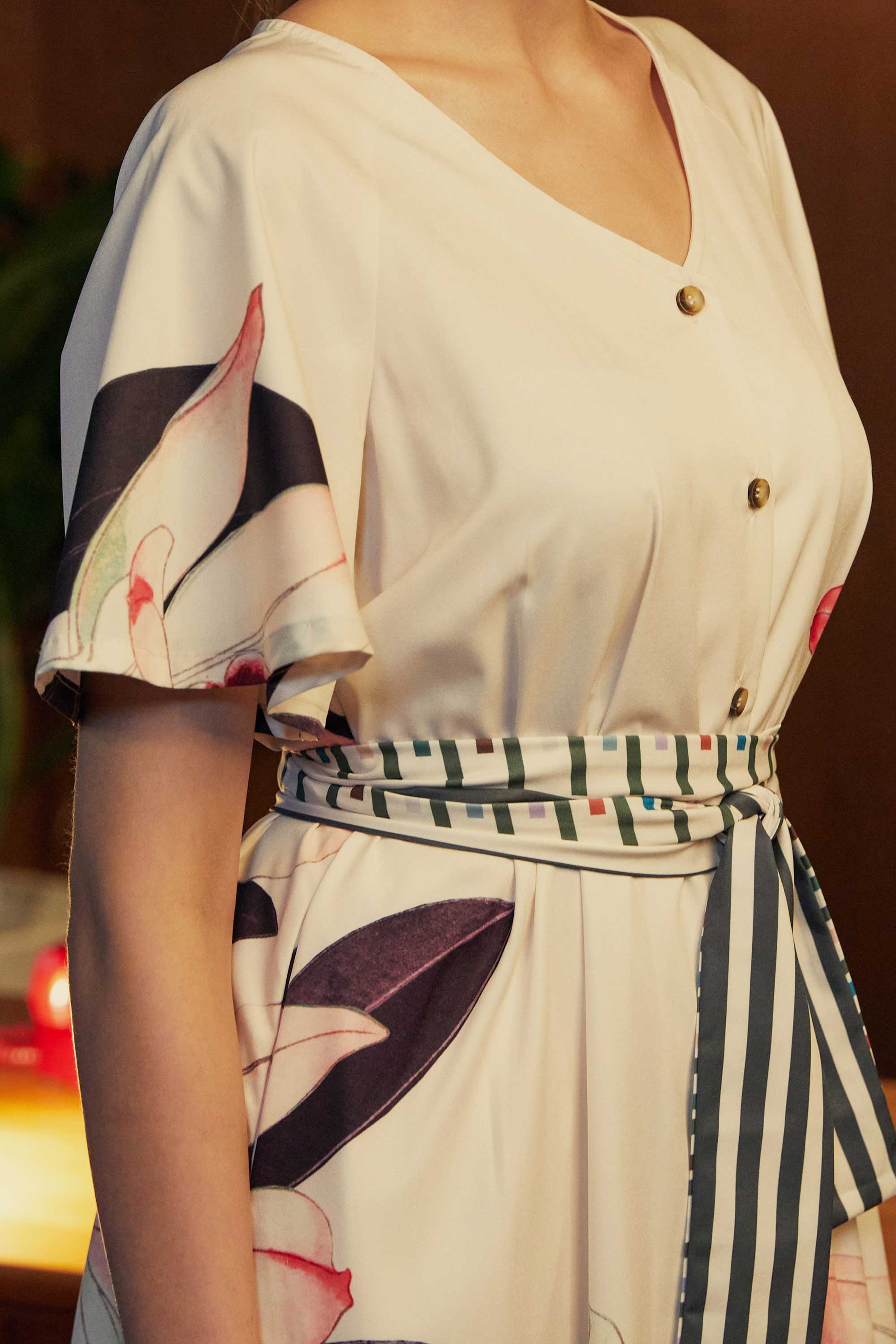 Close-up of the BEHOLD Flutter Sleeves Box Pleats Cinch Midi Dress in Dendrobium orchid print, featuring ivory fabric with bold floral motifs, striped cinched waist tie, button-down front, and flutter sleeve.