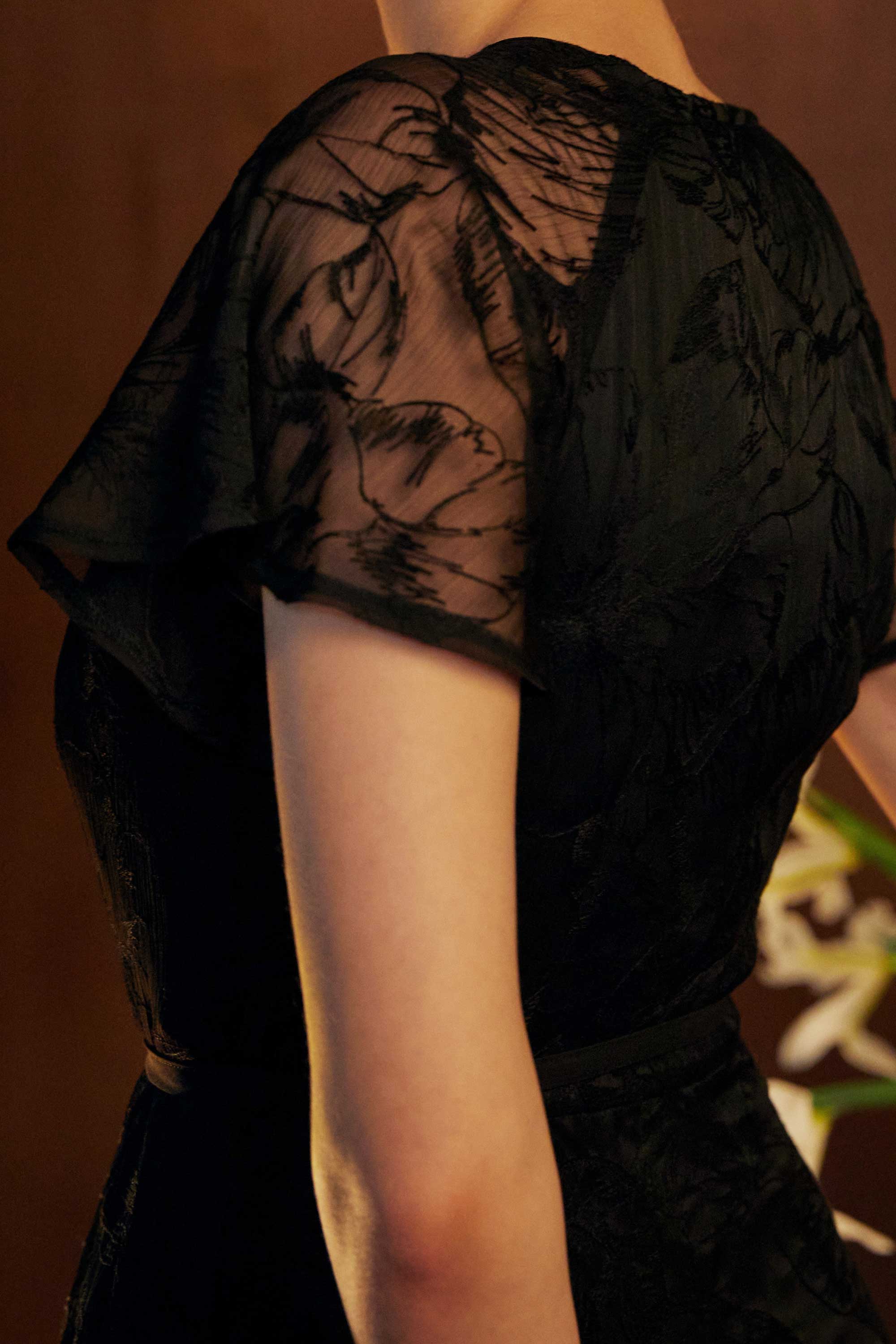 Close-up of the BEHOLD Flutter Sleeves Wrap Midi Dress in black lace, showing sheer flutter sleeve with delicate floral lace pattern and fitted waistline.