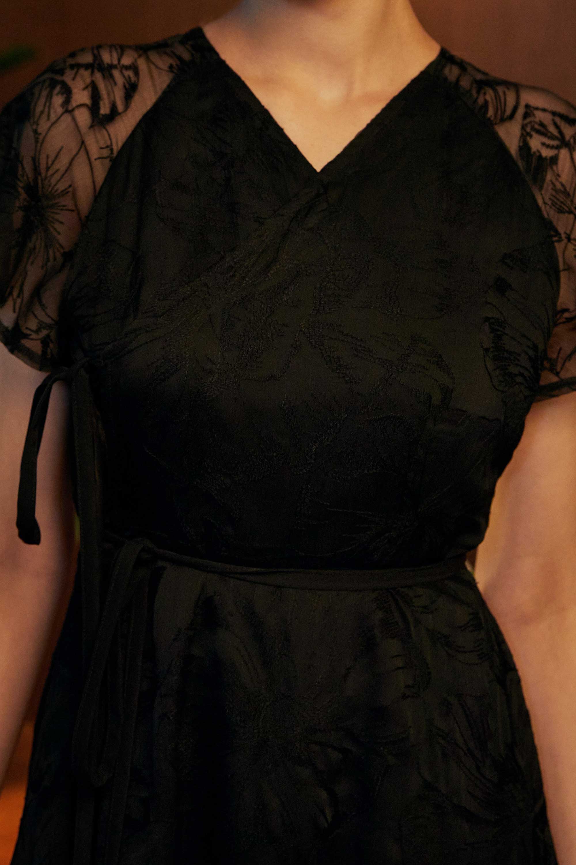 Close-up of the BEHOLD Flutter Sleeves Wrap Midi Dress in black lace, highlighting V-neckline, sheer floral lace sleeves, and wrap bodice detail.