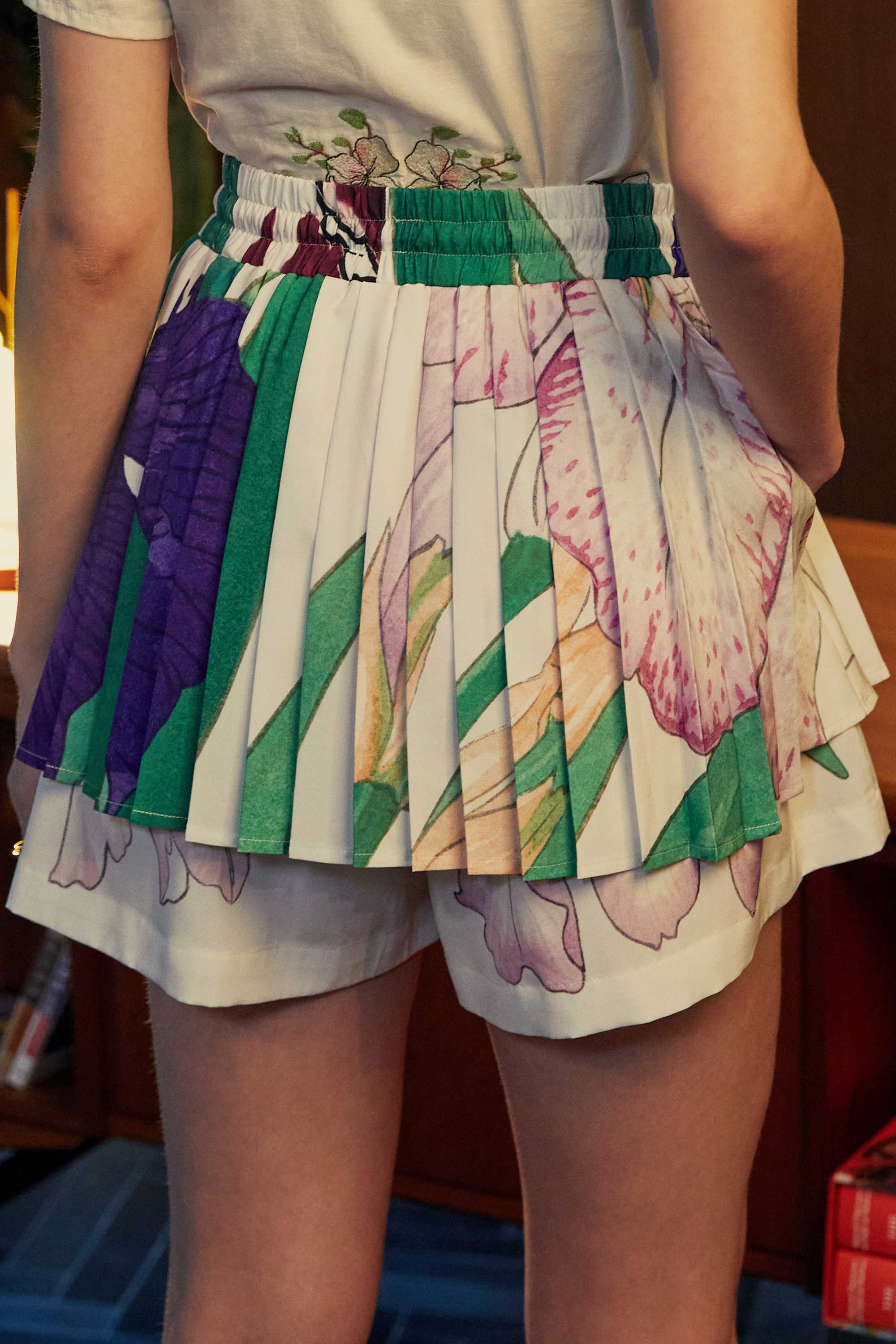 Back view of Iris-print twirl skorts featuring knife pleats, painterly florals in lilac and emerald, and integrated shorts for coverage.