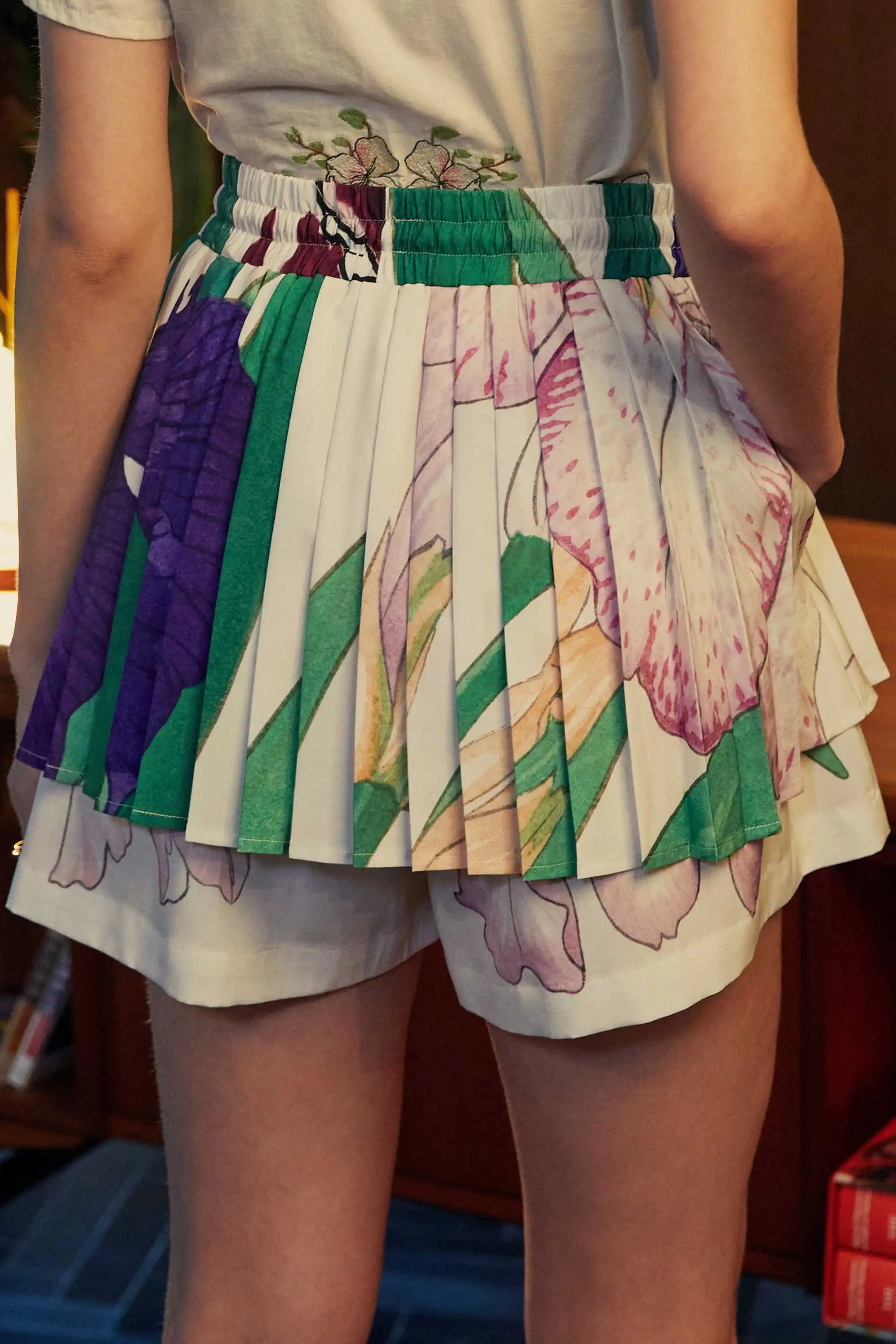 Back view of Iris-print twirl skorts featuring knife pleats, painterly florals in lilac and emerald, and integrated shorts for coverage.