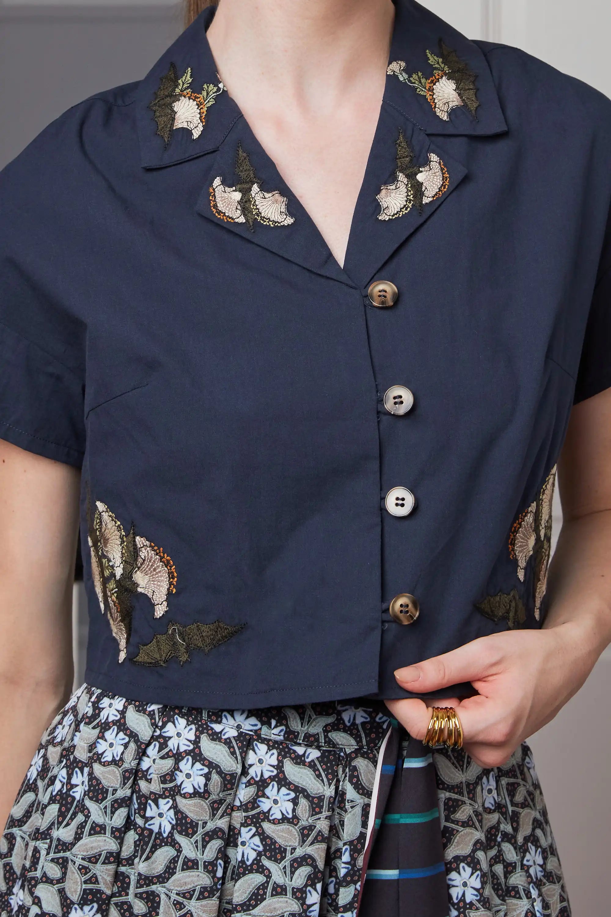 Close-up of embroidered navy cropped top highlighting front button placket, cropped cut, and Bat embroidery placement