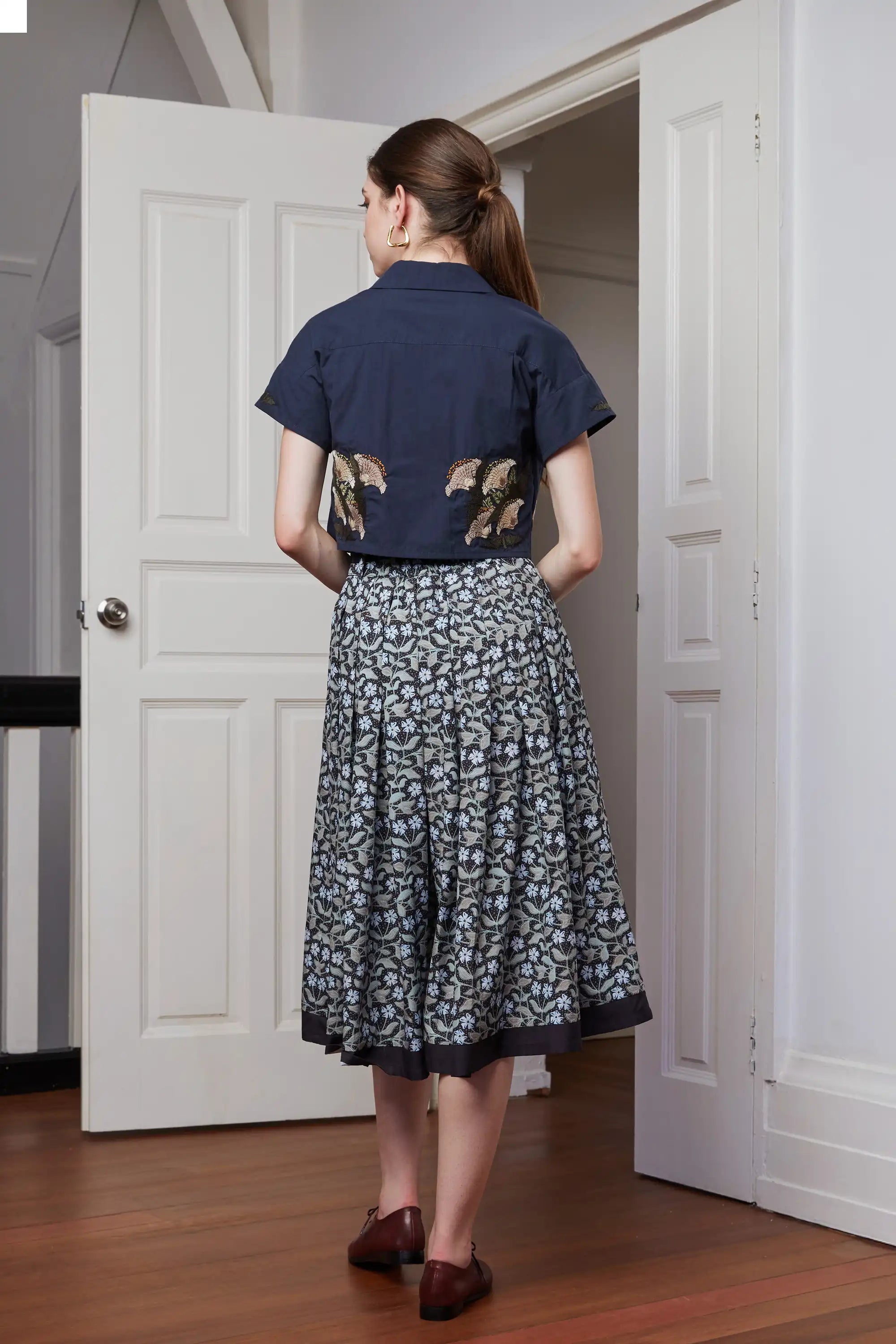 Full back view of wide leg pleated pants with gathered waistband and fluid volume, paired with cropped top for a balanced silhouette