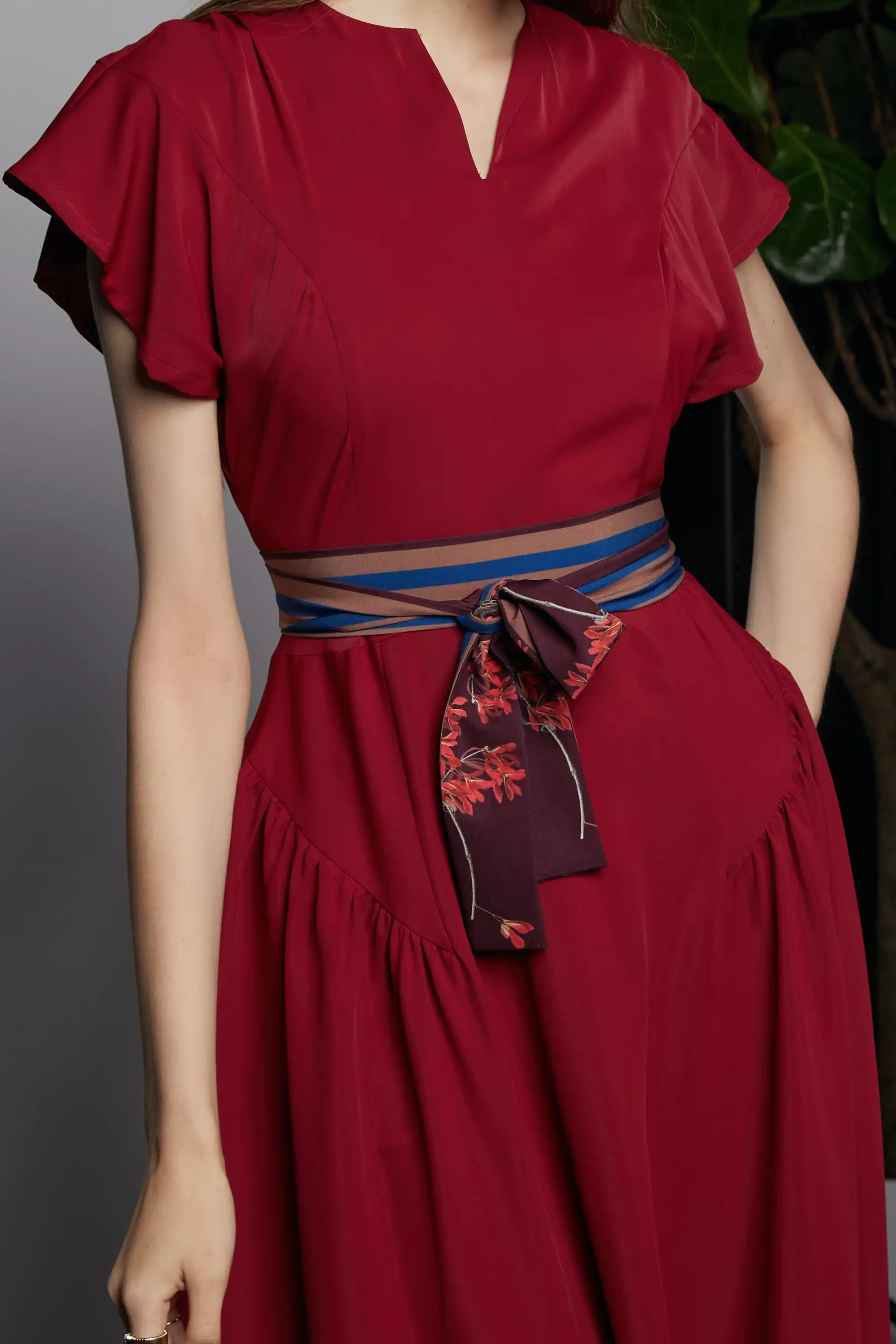Close-up of the HAVEN Bluebell Billowing Dress in deep red, highlighting the softly pleated bodice, flutter sleeves, and signature striped sash belt in the Java Sparrow print. The belt features a contrasting maroon section with delicate red floral accents, tied at the waist to accentuate the silhouette.