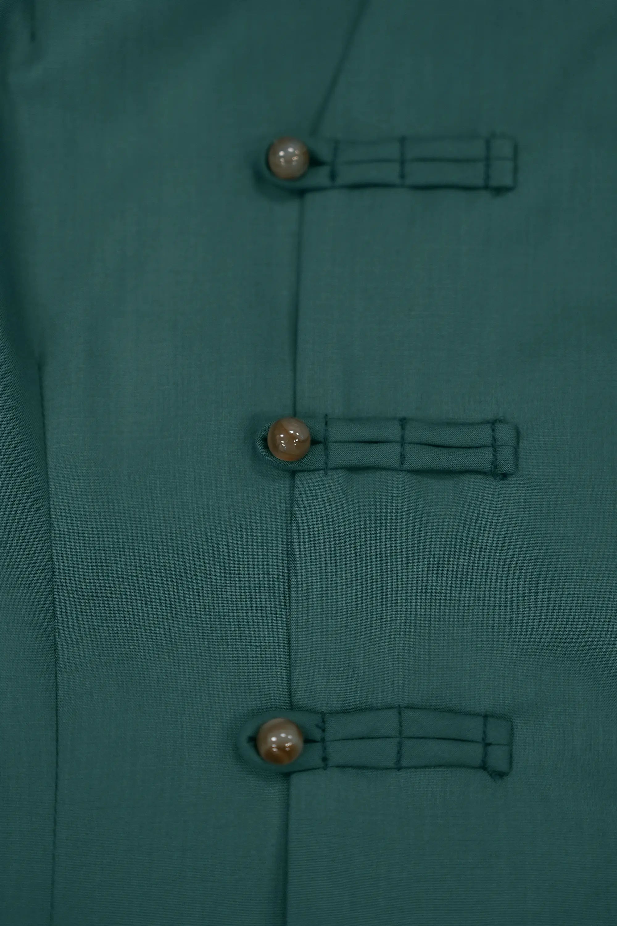 Close-up of deep green top featuring handcrafted pankou button closures, smooth fabric texture, and refined traditional detailing