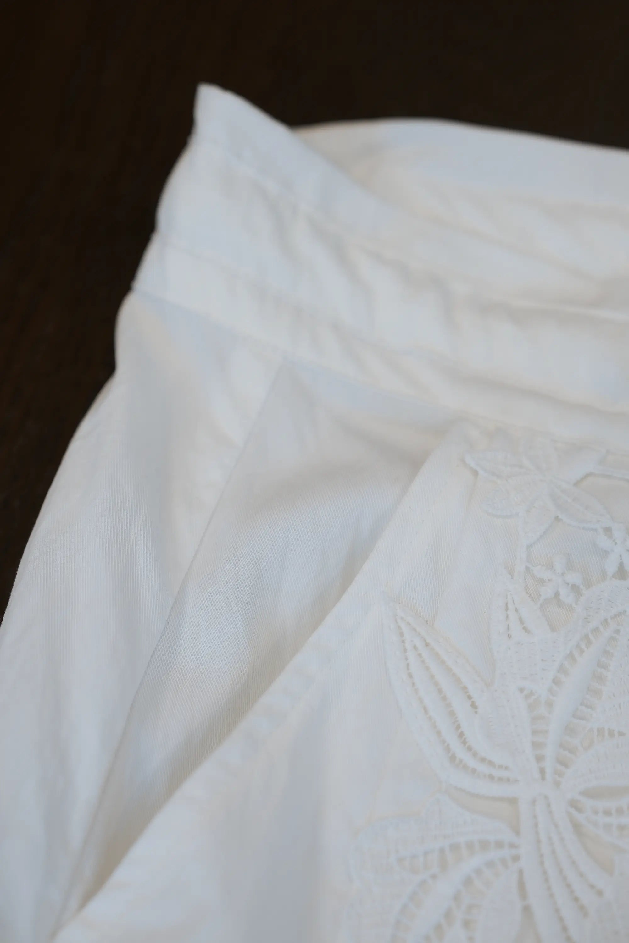 Close-up of white palazzo pantds showing soft pleat detail and contrast between smooth fabric and embroidered lace panel