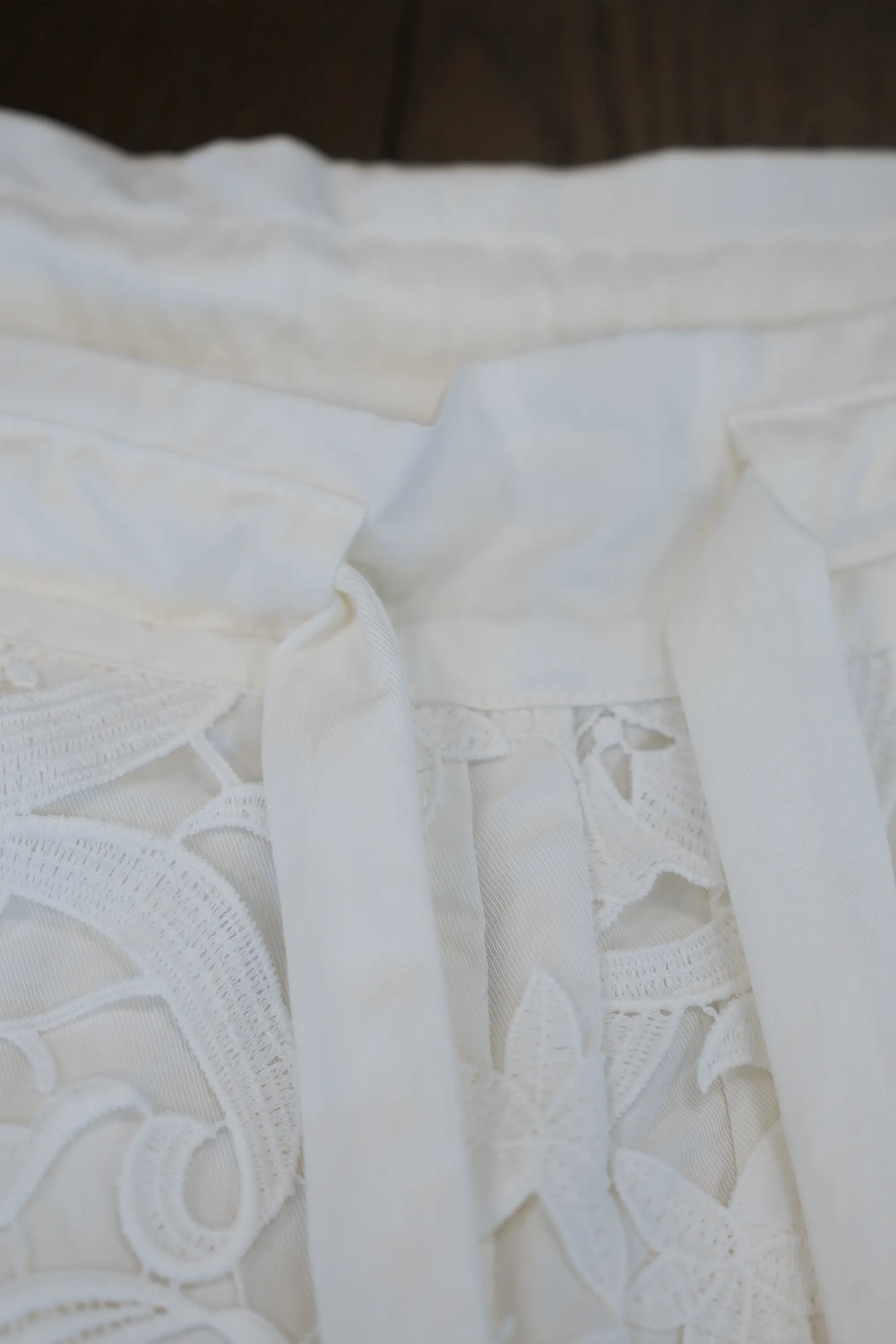 Close-up of white palazzo pants showing gathered waistband with adjustable tie and floral lace panel detail