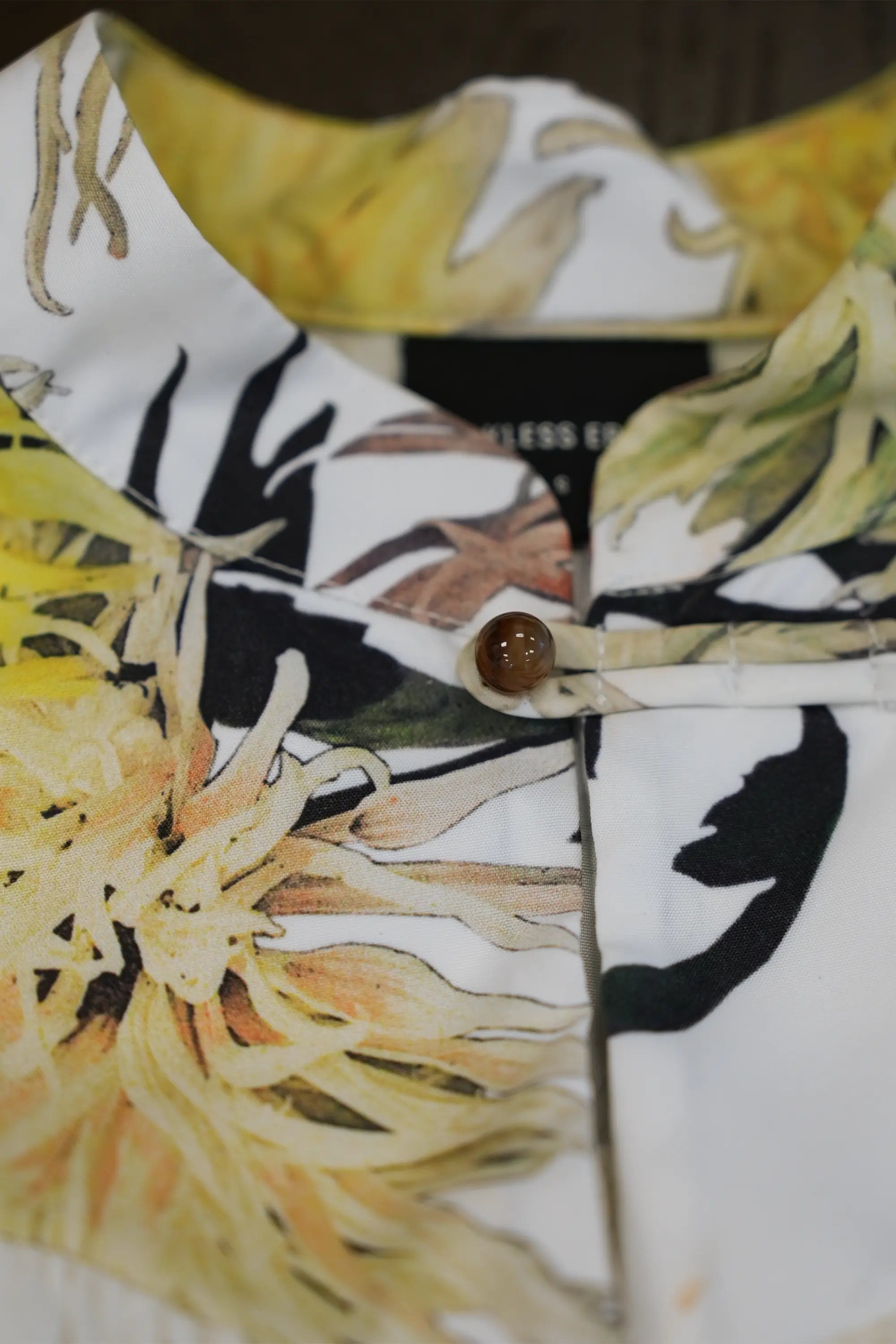 Close-up of high floral printed collar featuring chrysanthemum motifs in soft yellow and earthy tones, finished with a polished button detail and clean neckline construction