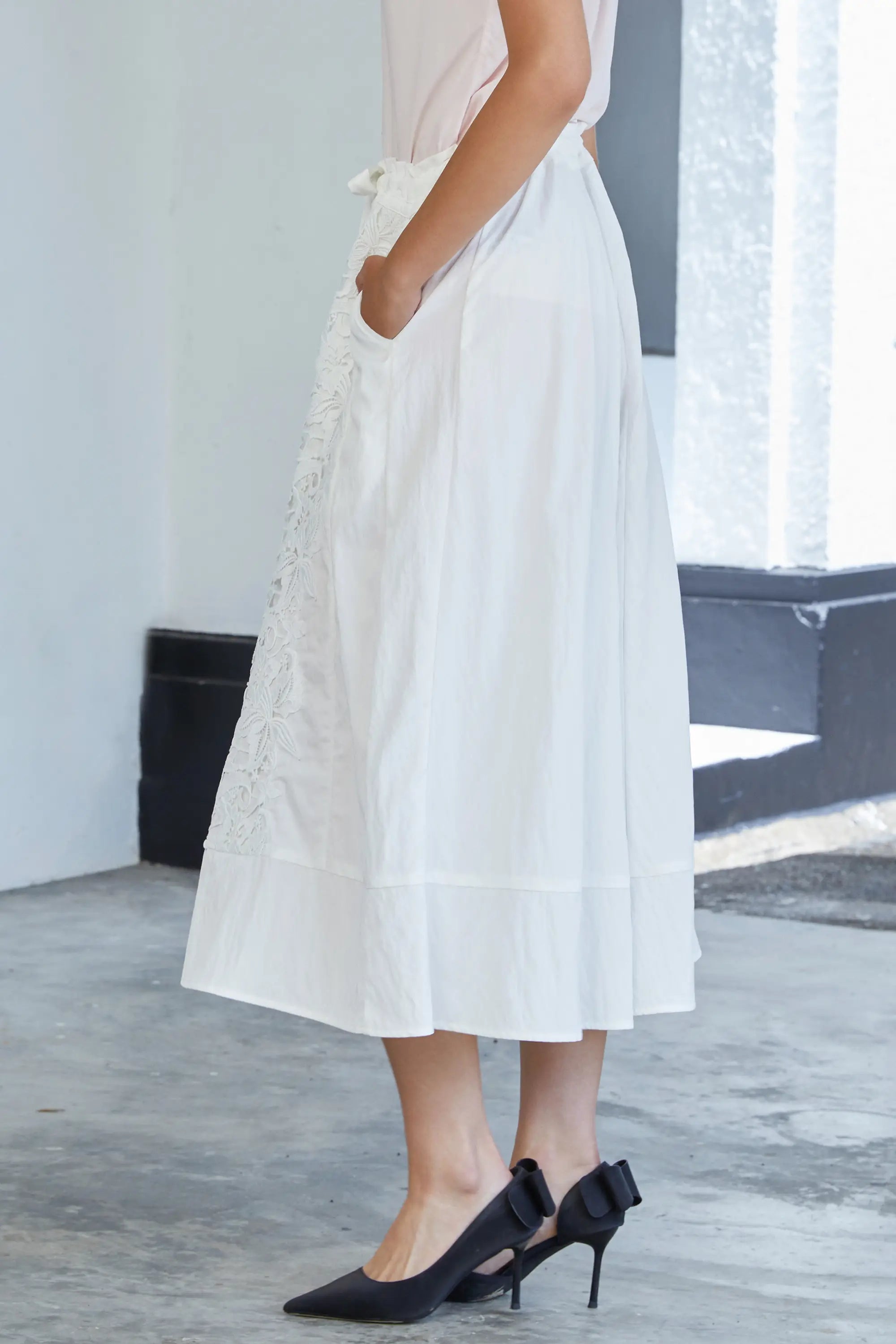 Woman wearing ABIDE white lace wide-leg pants with waist tie and soft drape (side view)