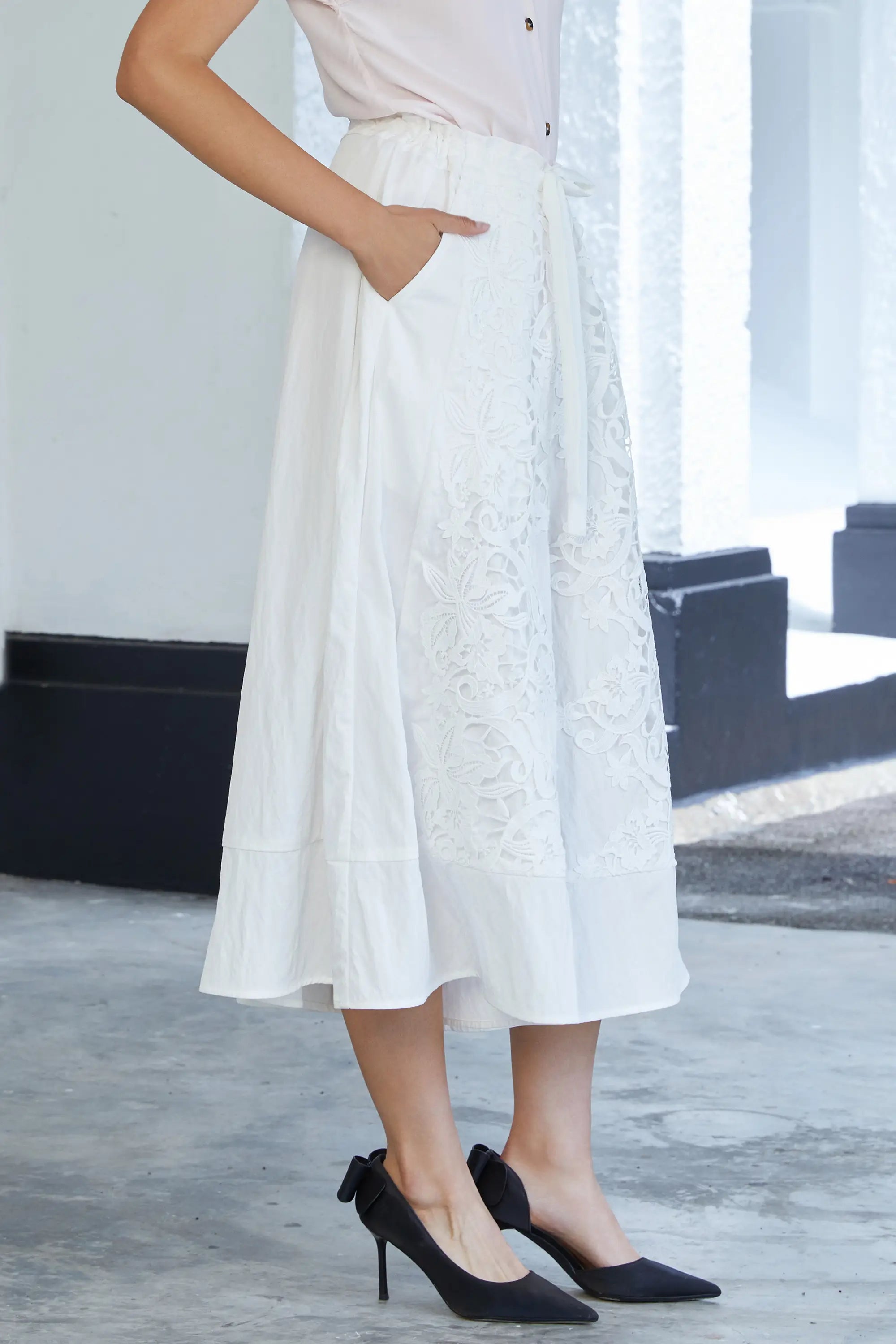 Woman wearing ABIDE white lace wide-leg pants with waist tie and soft drape (side view)