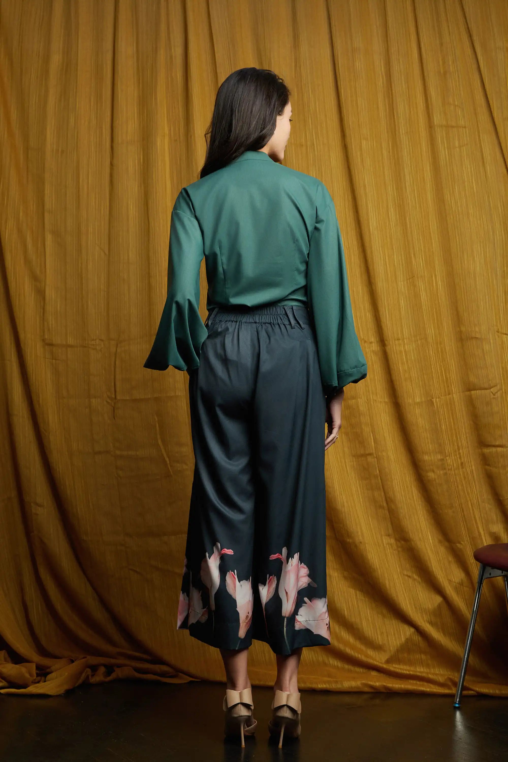 Deep green long-sleeve top with smooth back and relaxed fit, paired with dark pleated slit pants featuring structured waistband, belt loops, and flowing wide-leg silhouette with floral hem accents