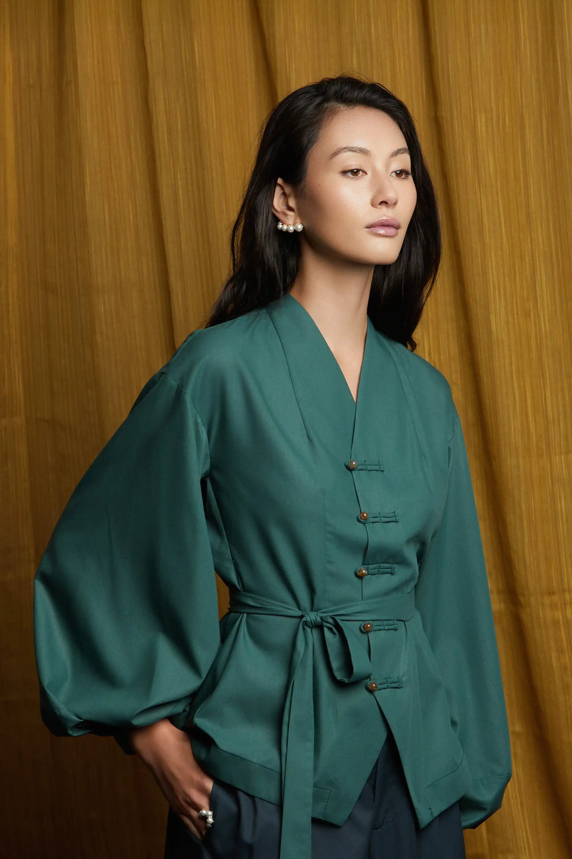 Deep green top with clean side profile, fluid sleeves, and waist-cinching sash tie that enhances shape and movement