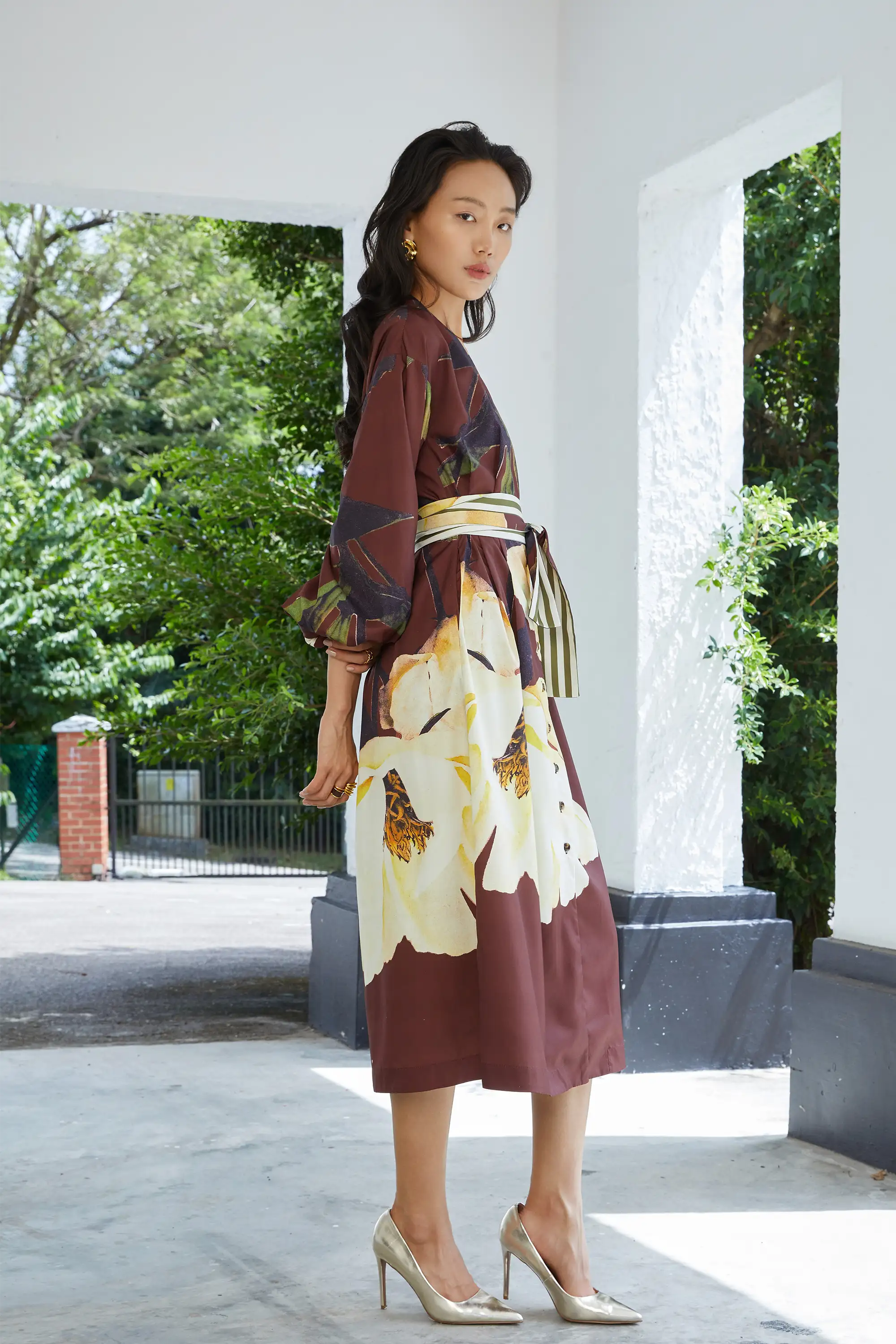 Woman wearing ABIDE brown floral midi dress with contrast sash belt (side view)