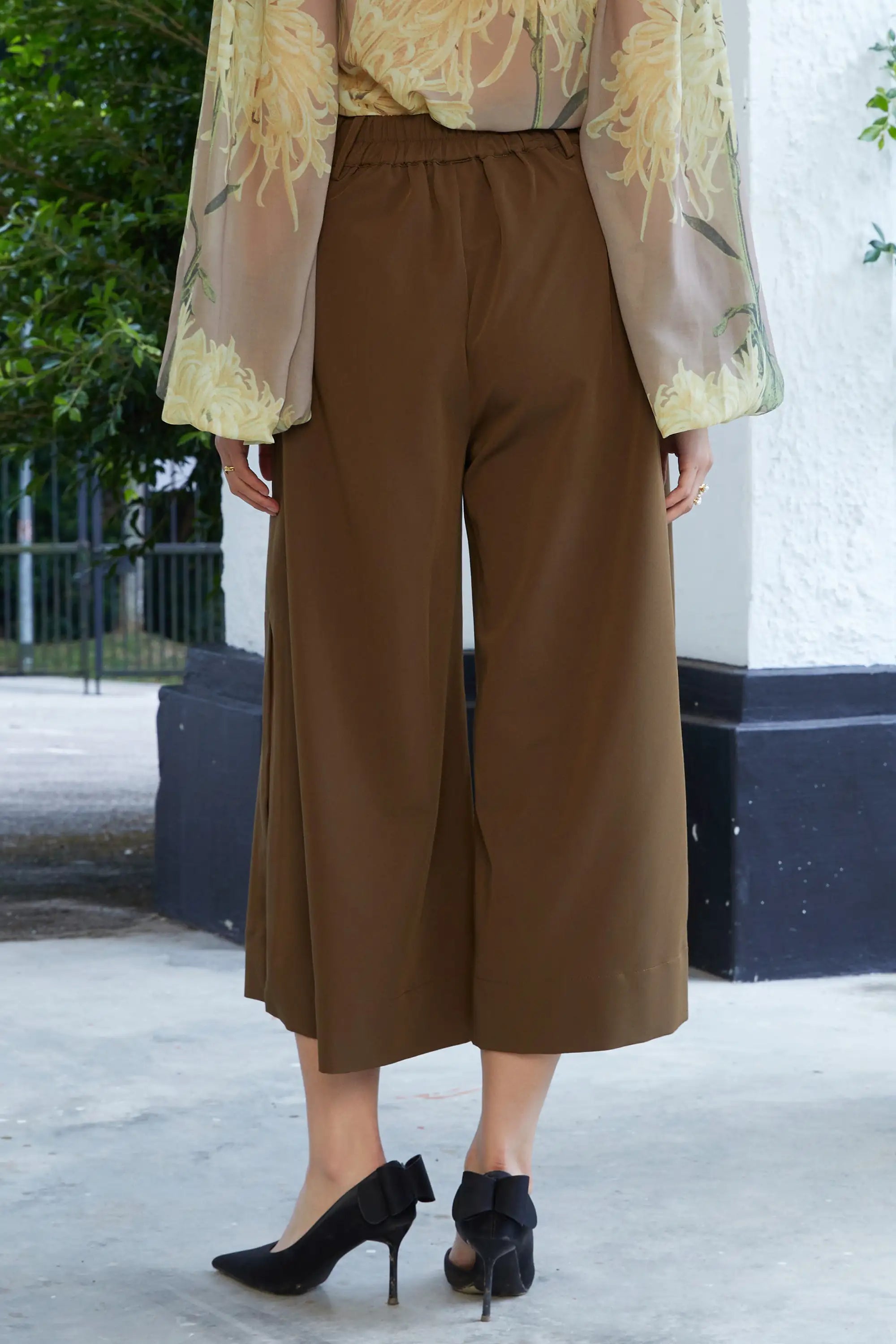 Woman wearing ABIDE brown pleated slit wide-leg pants outdoors (back view)