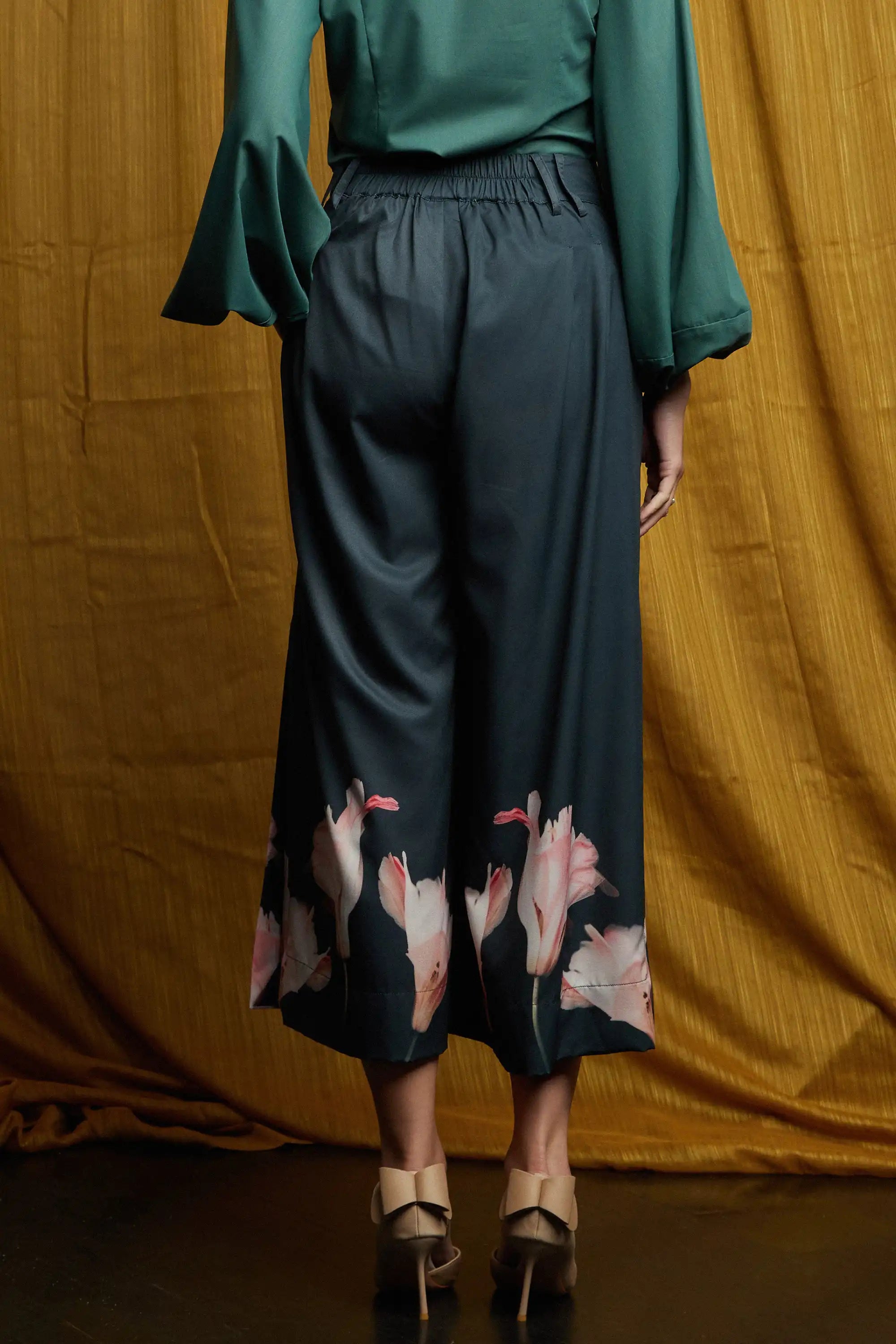 Deep green long-sleeve top with smooth back panel and easy fit, paired with dark pleated slit pants featuring a structured waistband, belt loops, and full silhouette with floral hem detail