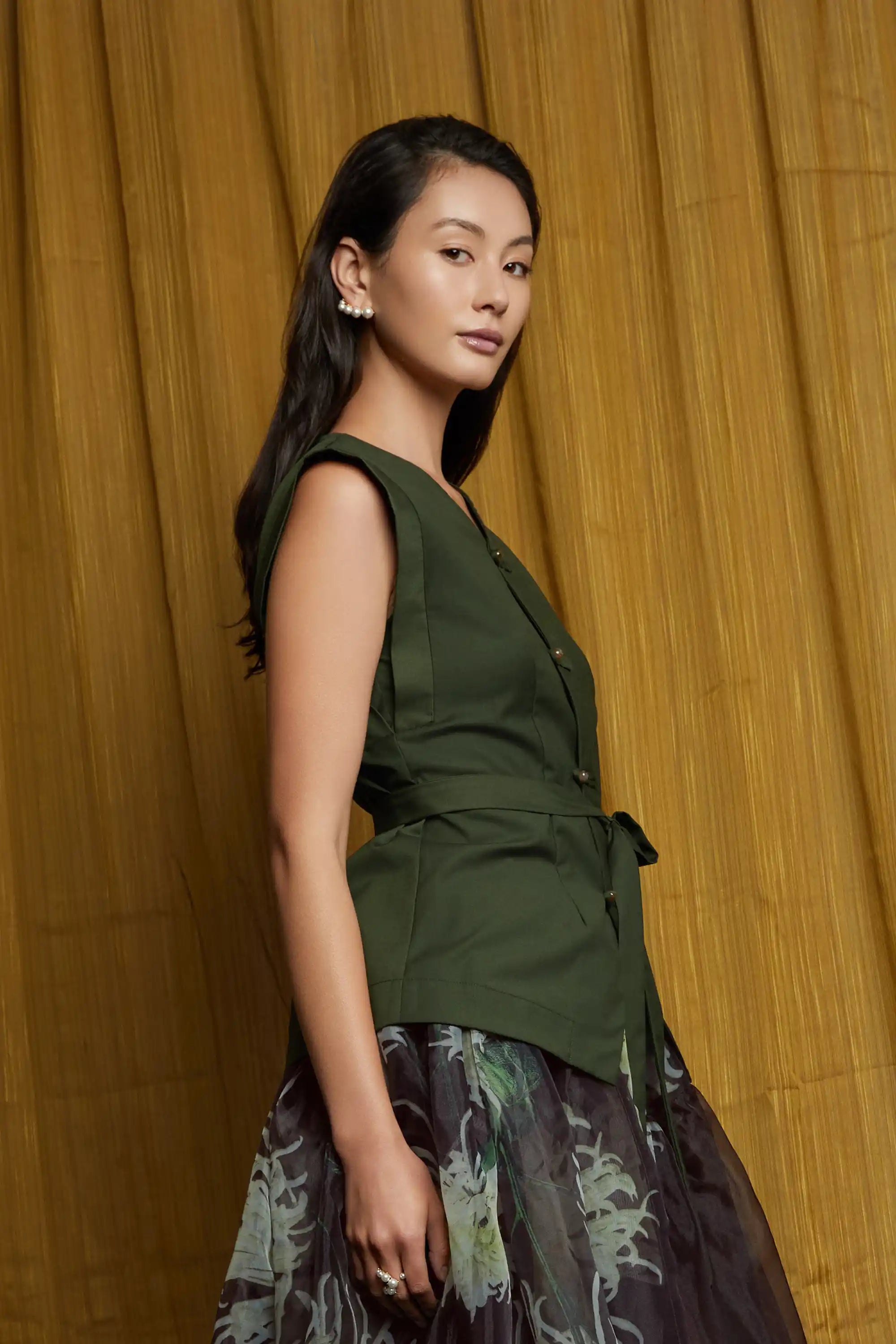 Deep green structured top with clean lines and subtle shoulder structure, styled with a sheer floral skirt, showcasing fluid drape and airy volume from the side