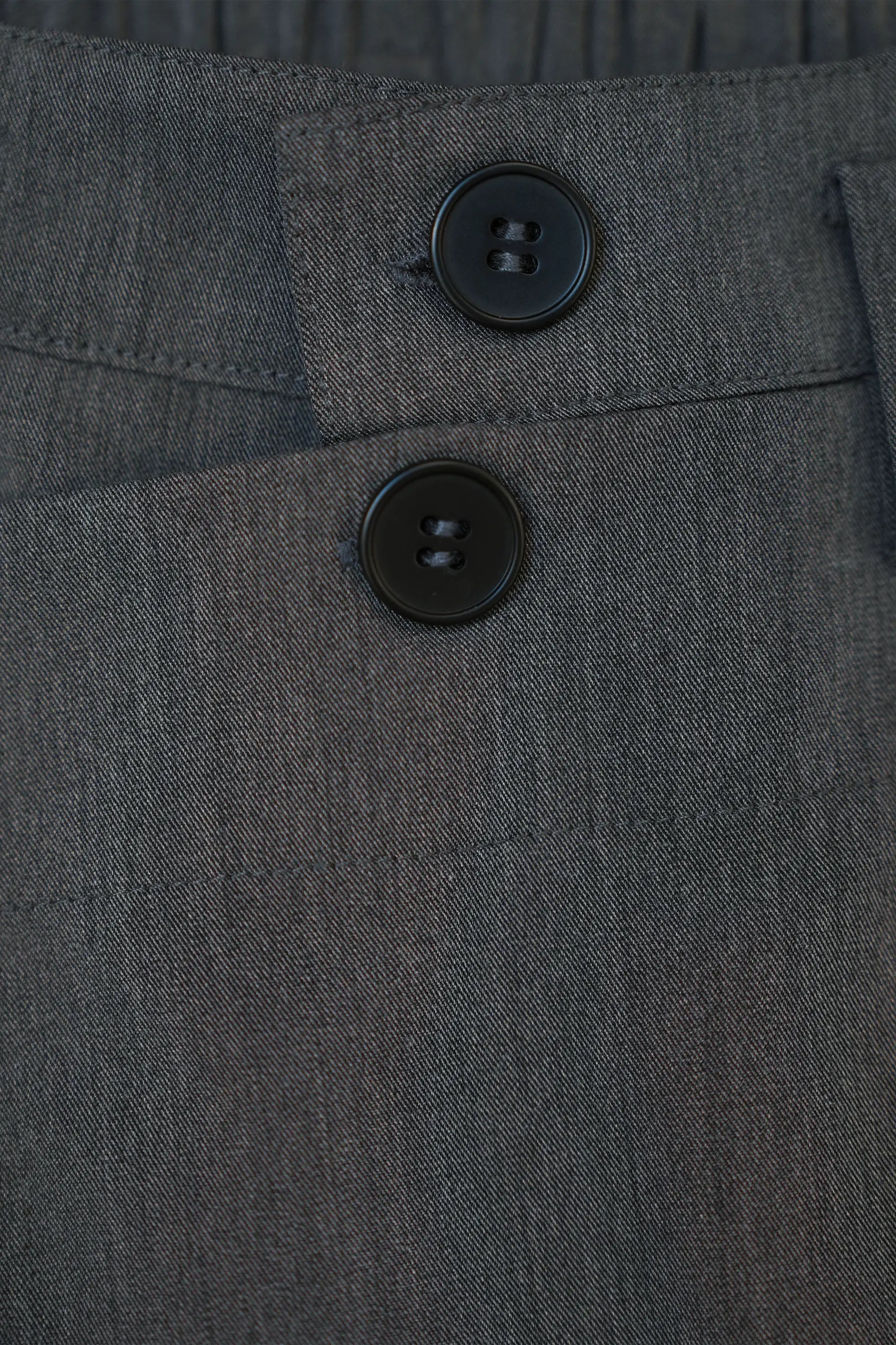 Close-up of button and zip closure on Arrayed dark grey wrap trousers