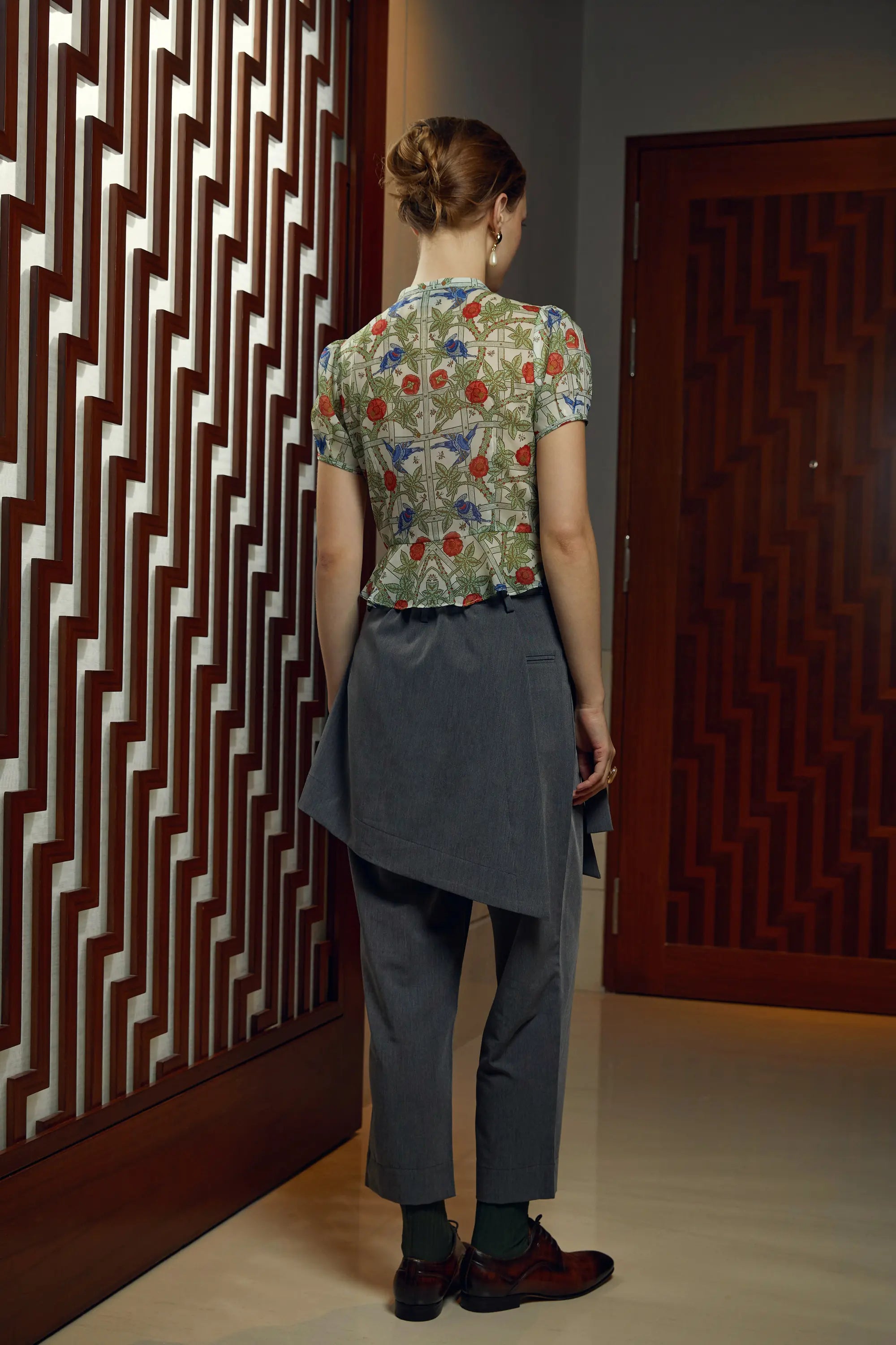 Woman wearing Arrayed Trellis keyhole peplum top with dark grey wrap trousers, back view