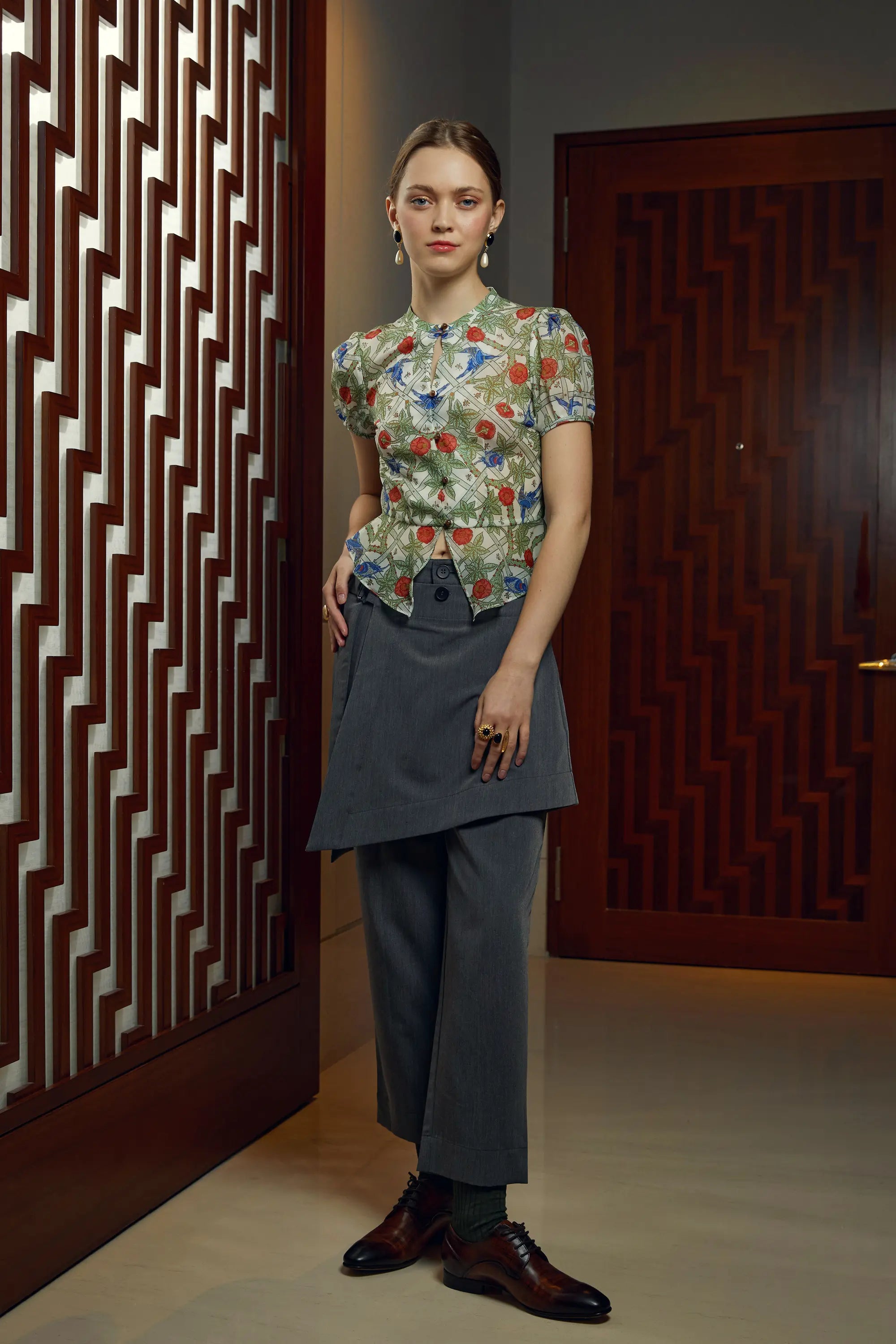 Woman wearing Arrayed Trellis keyhole peplum top with dark grey wrap trousers, front view