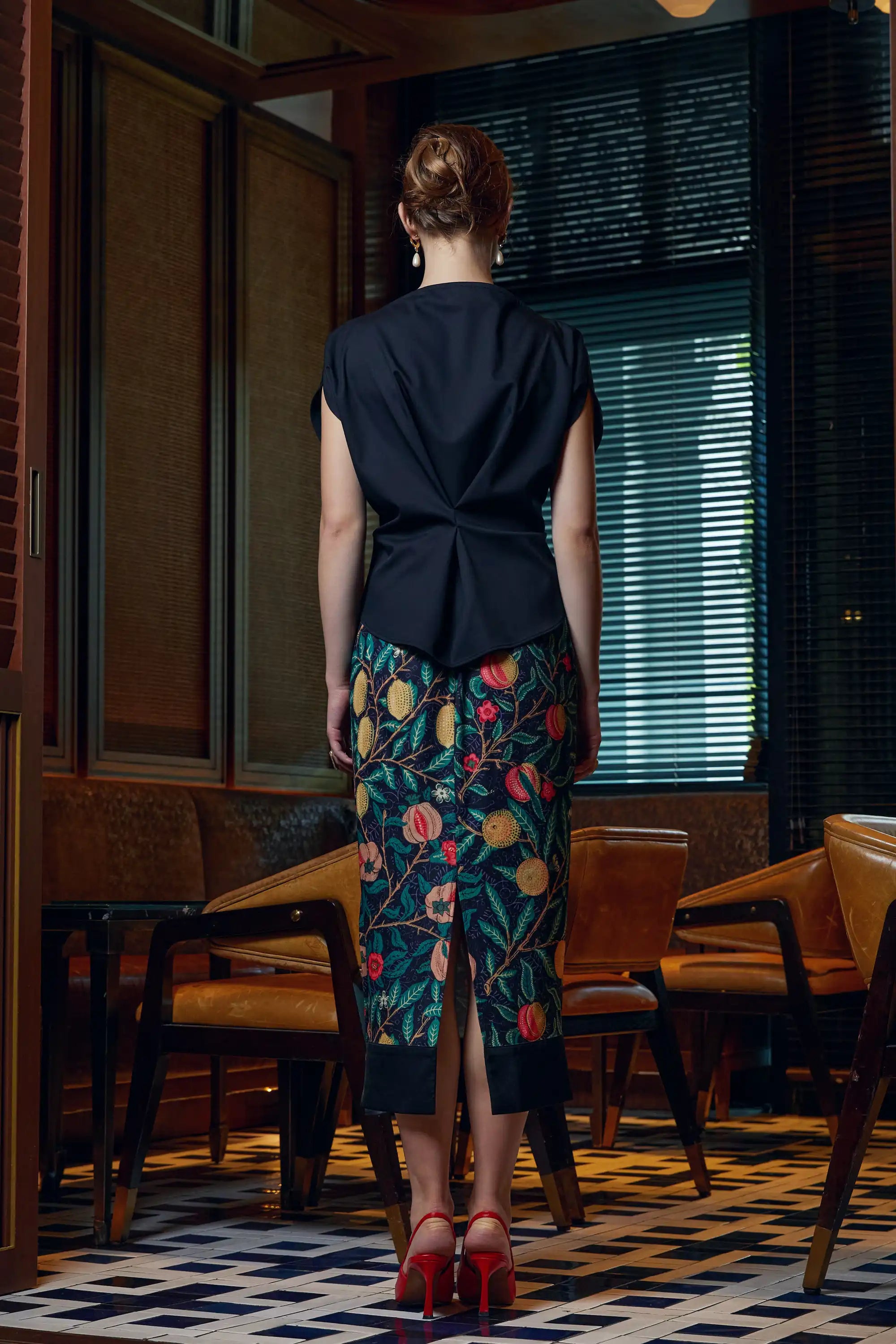 Woman wearing adjustable black top with Arrayed Pomegranate print ribbed midi skirt, back view