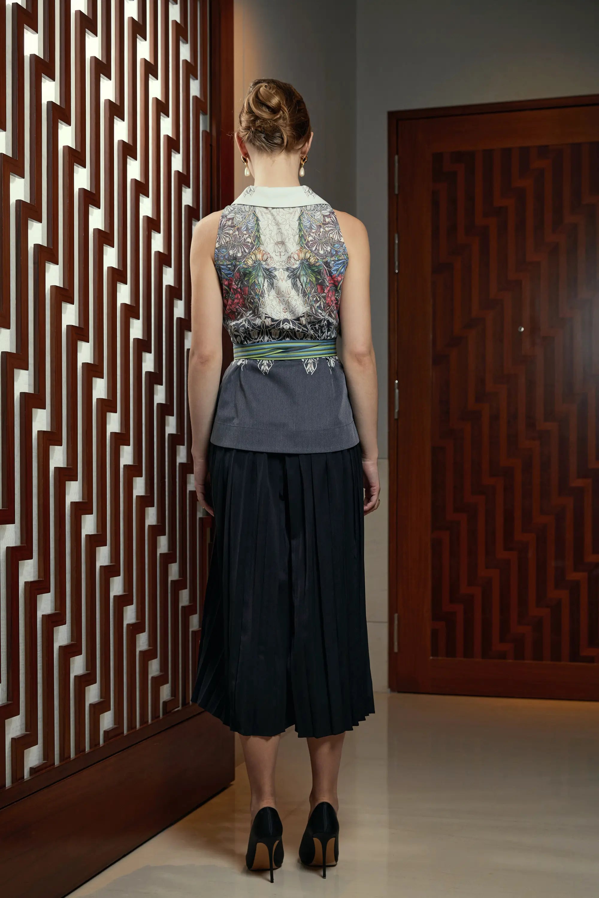 Woman wearing Arrayed Honeysuckle shawl collar top with black pleated skirt trousers, back view