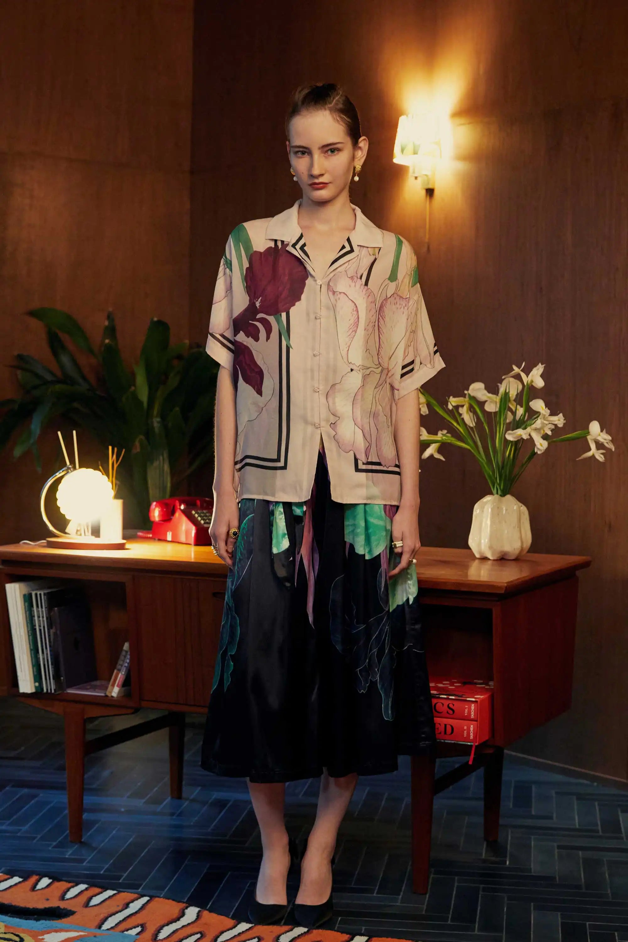 Model wearing Reckless Ericka’s oversized Cuban shirt with bold iris print, styled with high-waisted paperbag palazzo pants — shot in a mid-century room with warm lighting and tropical greenery.