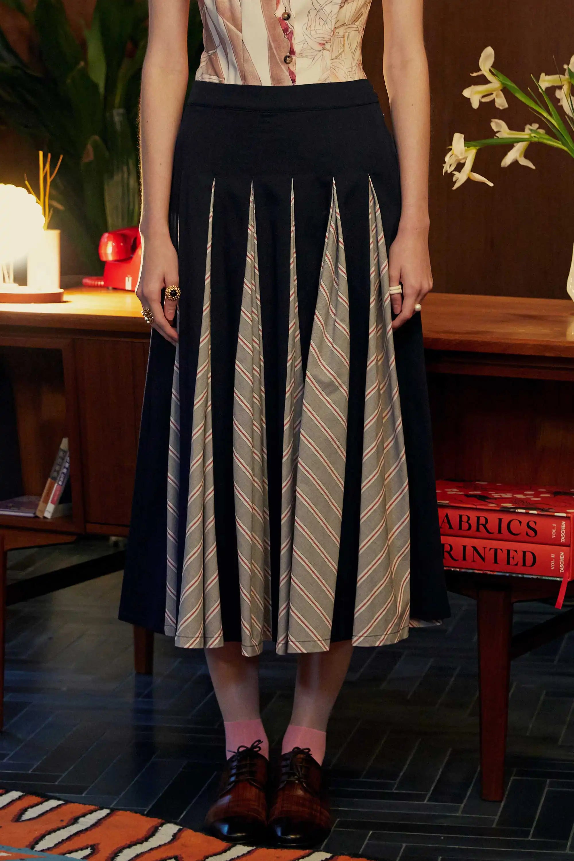 Front view of the Godet Skirt in Navy Red, featuring structured navy panels and beige chevron-striped godets, styled with oxford shoes and pink socks.
