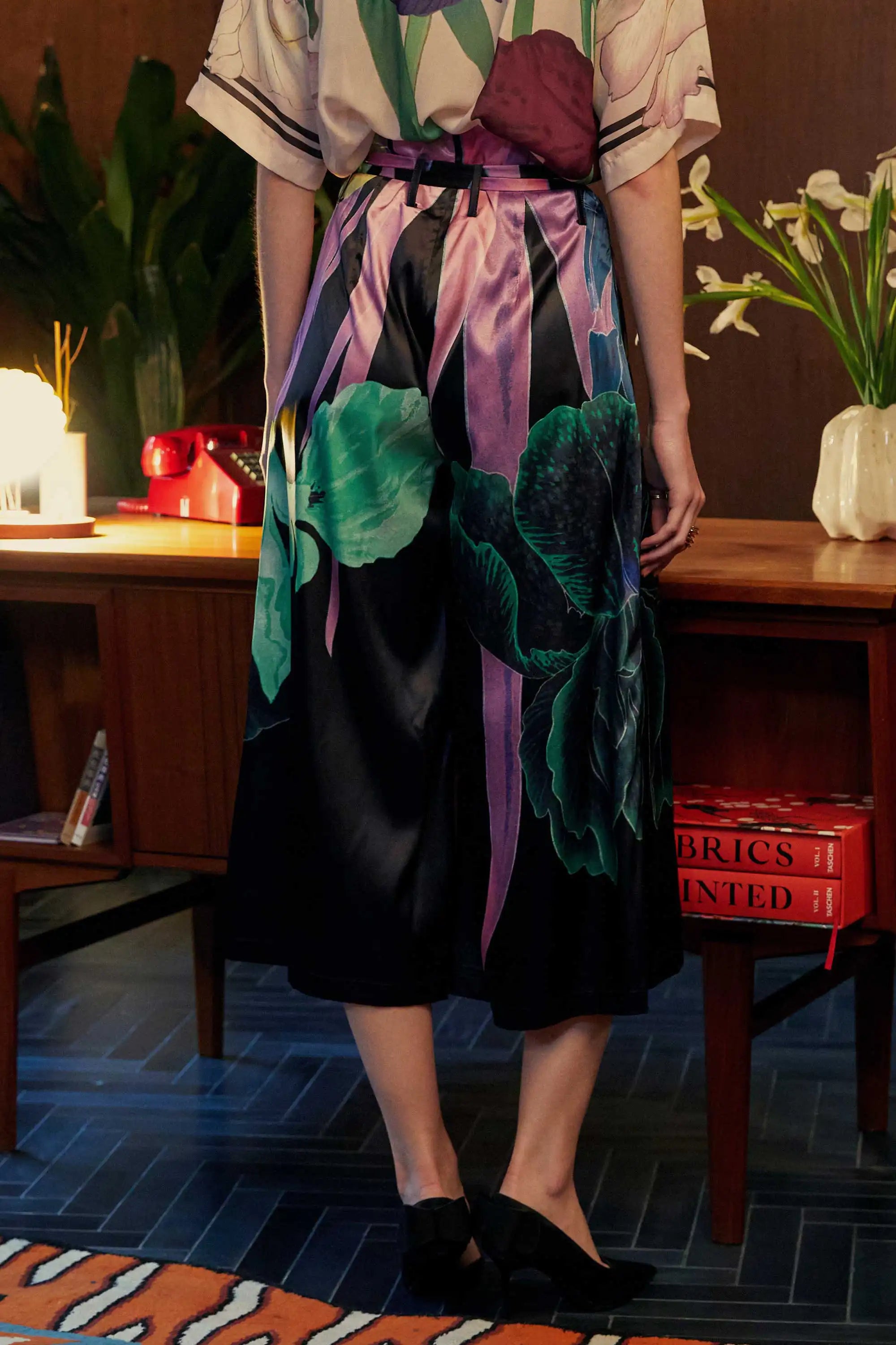 Back view of black satin paperbag palazzo pants from Reckless Ericka — featuring oversized iris prints in jewel-toned greens and purples, styled with gathered waist and full volume silhouette.