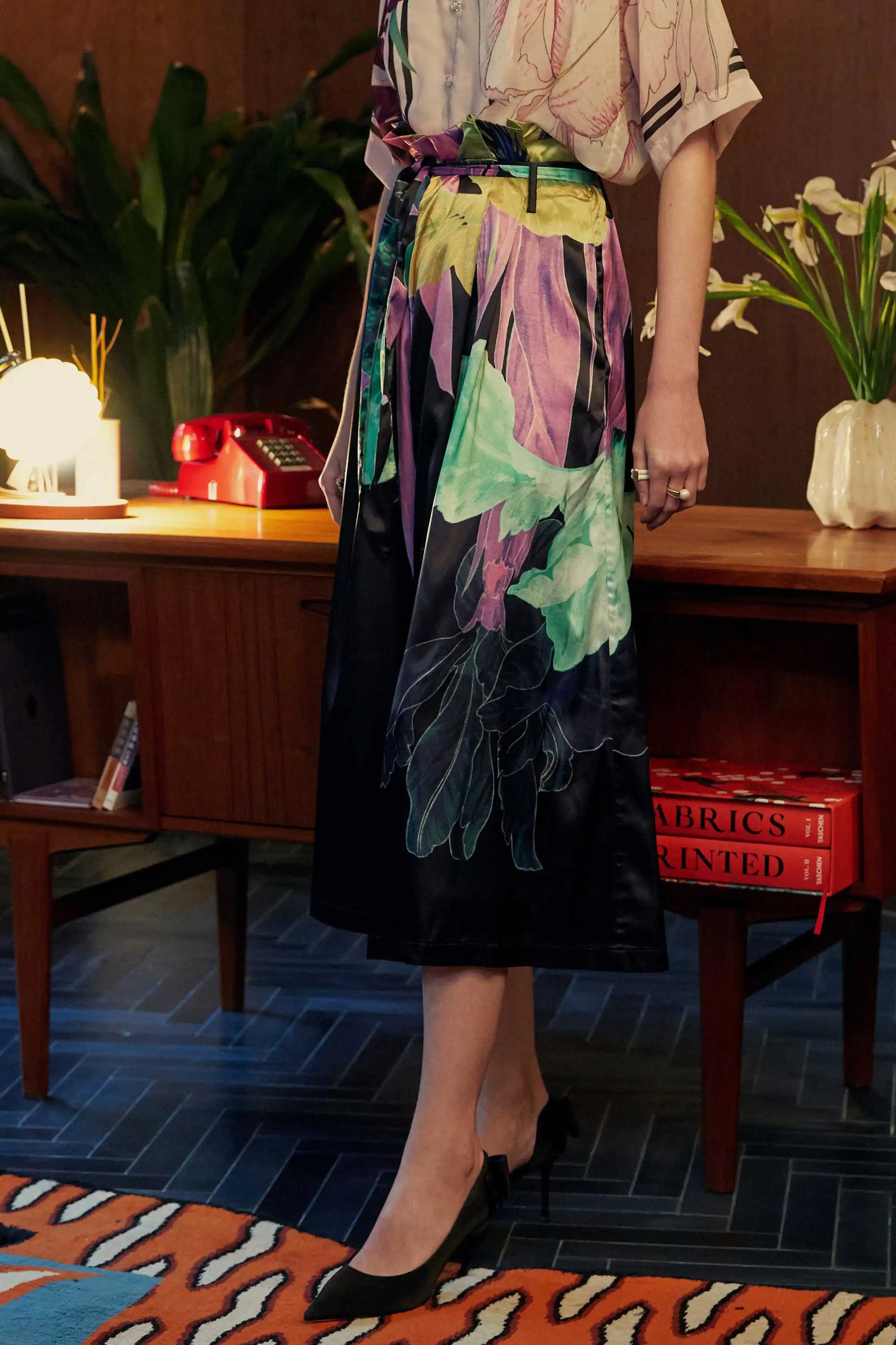 Side view of BEHOLD paperbag palazzo pants in Iris print by Reckless Ericka, featuring oversized botanical motifs in deep plum, mint, and orchid hues — styled in an indoor vintage-inspired setting.