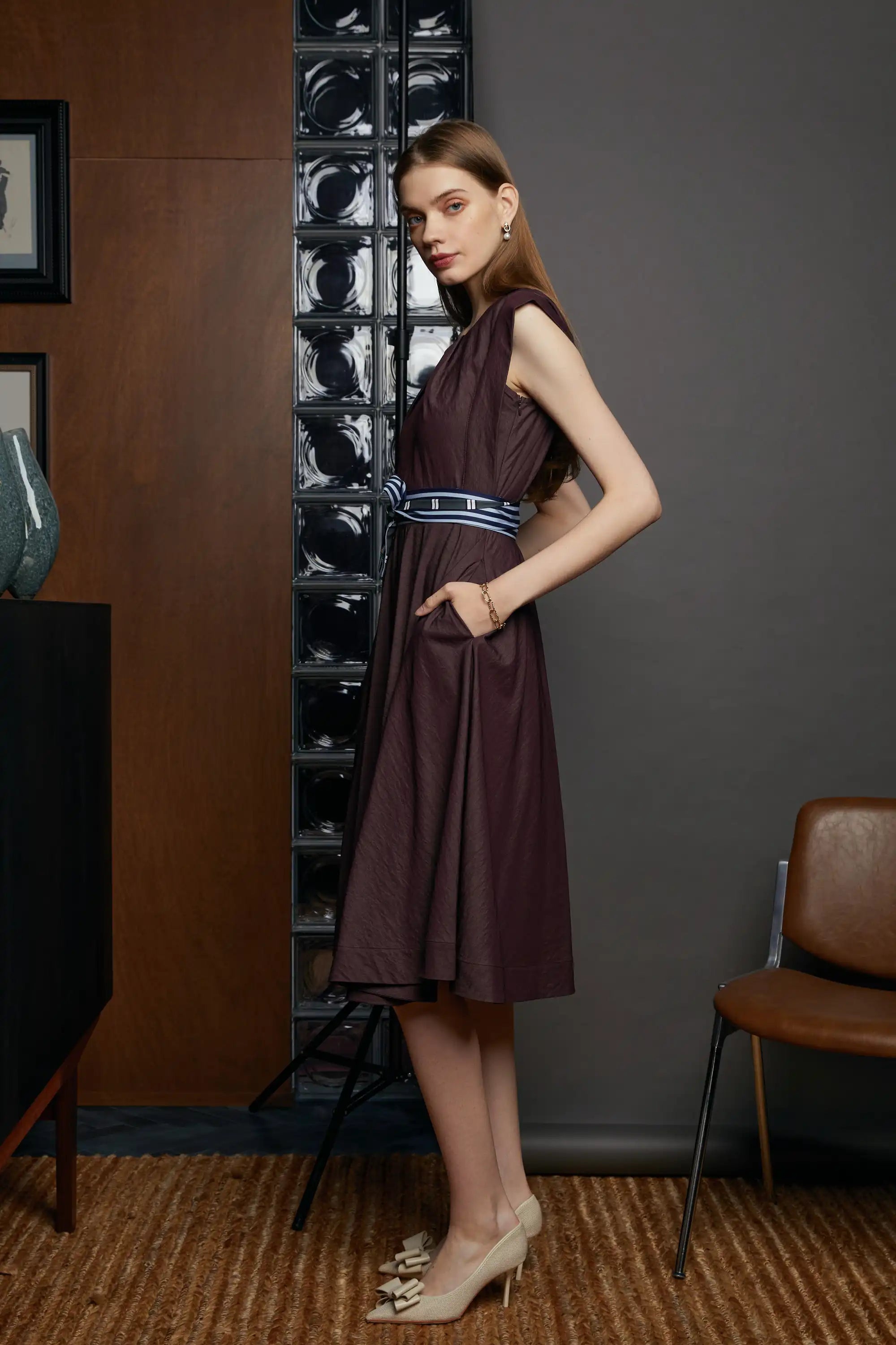 Side profile of a sleeveless midi dress with structured square shoulders, contrast sash belt, and softly flared skirt.
